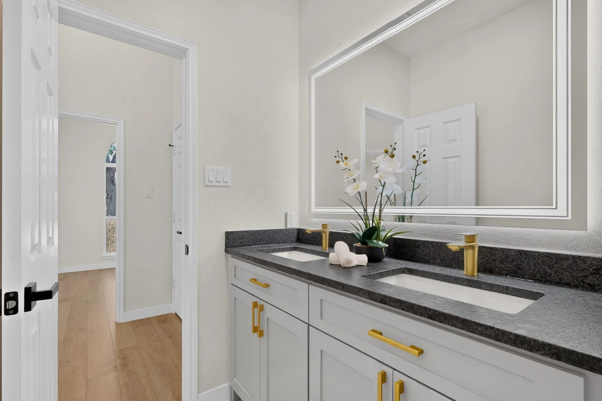 Dual vanity with undermount sinks, gold-finish fixtures, dark countertop, and integrated mirror lighting
