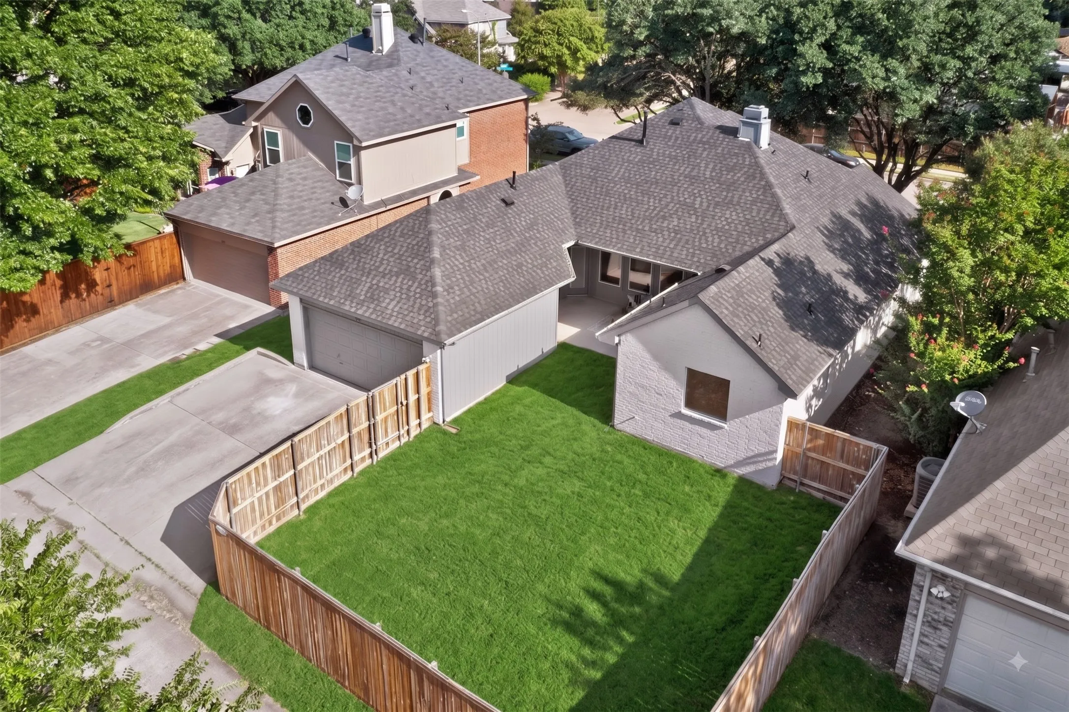 Expansive grassy yard with wood fencing, a concrete patio, and an attached garage with a shingle roof
