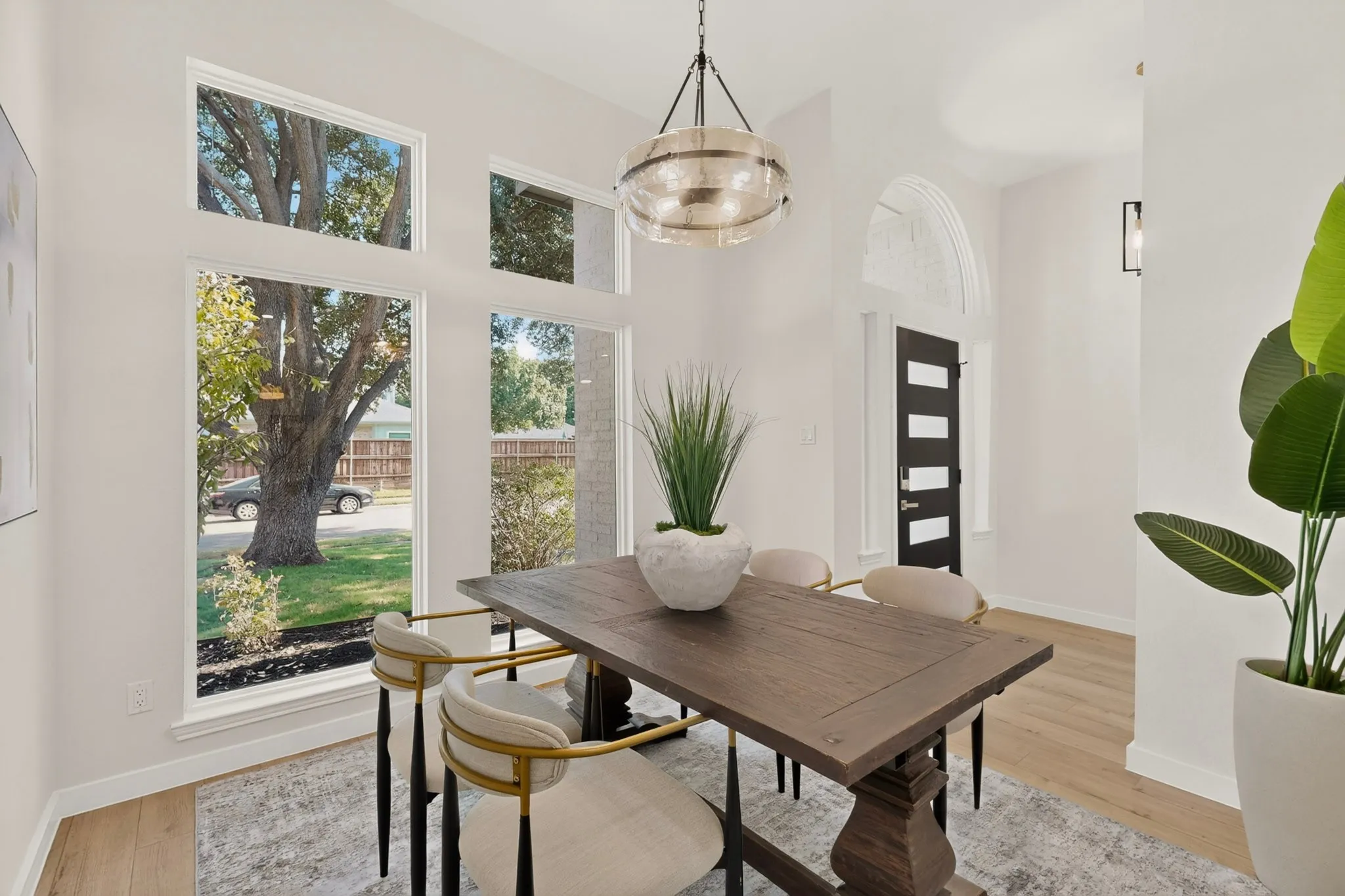 Light wood-finish flooring, multiple large windows, arched entryway detail, and modern ceiling light fixture