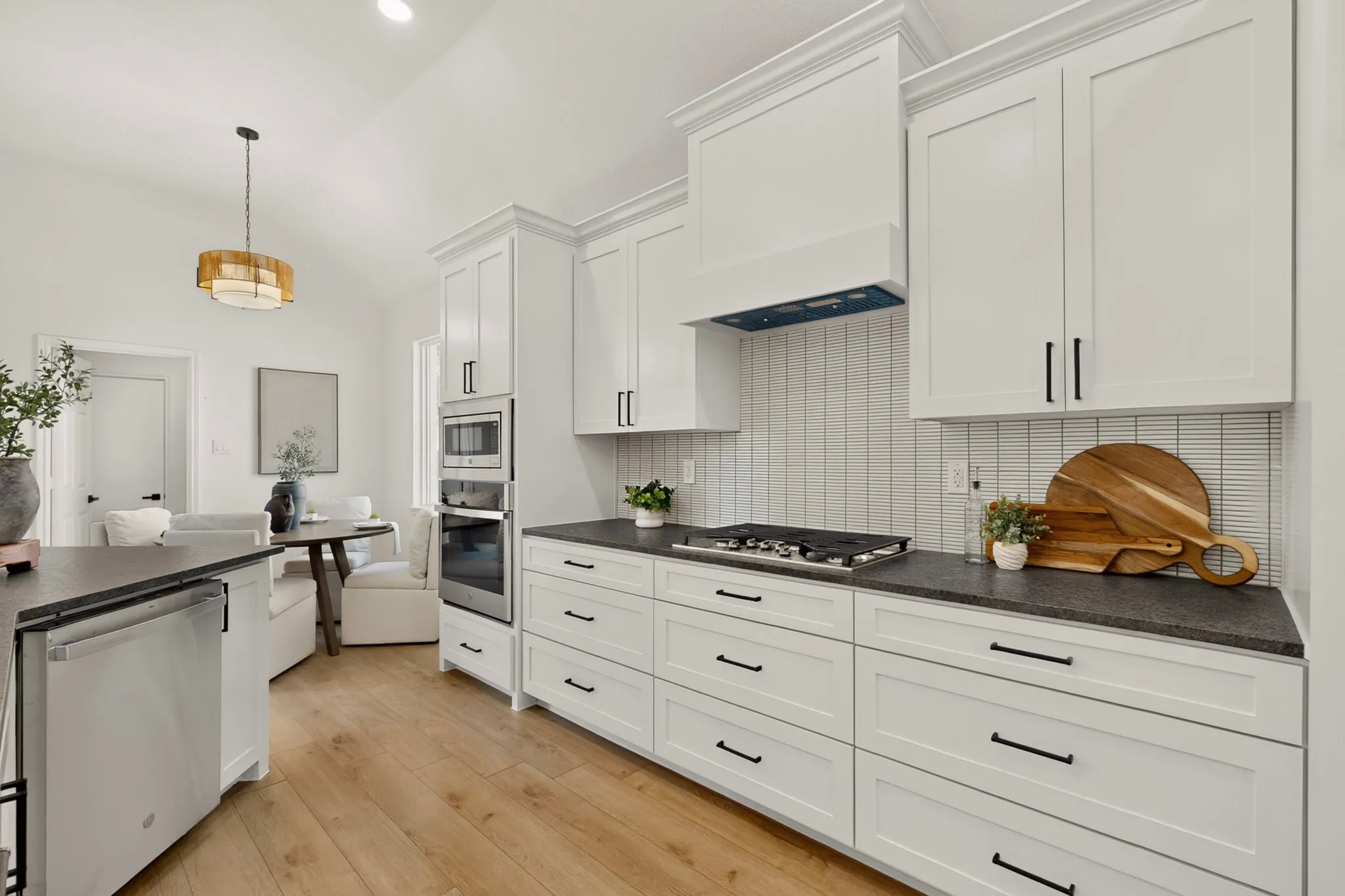 White shaker cabinetry with black hardware, built-in stainless steel appliances, dark countertops, a gas range, and wood-finish flooring