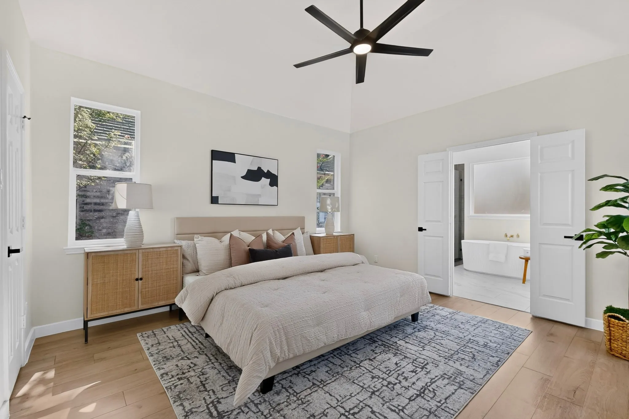 Vaulted ceiling with a black ceiling fan, wood-finish flooring, and white paneled doors opening to a bathroom with a freestanding tub