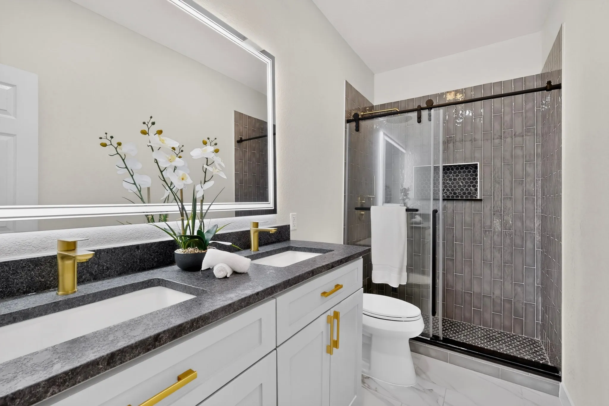Dual vanity with dark stone-finish countertop, gold-finish fixtures, and integrated sinks