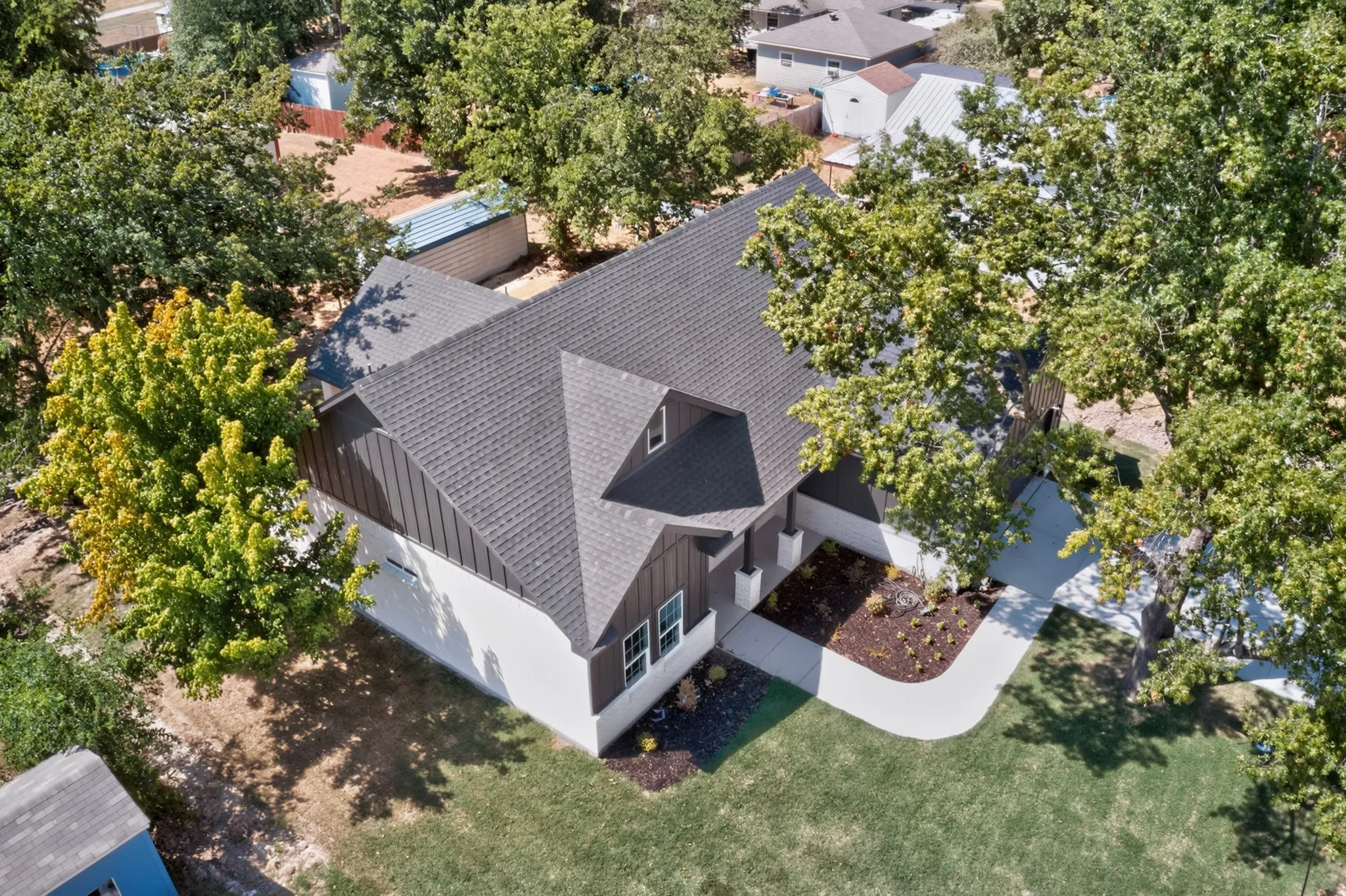White exterior with dark trim, prominent gabled roofline, dormer window, and mature trees on the property