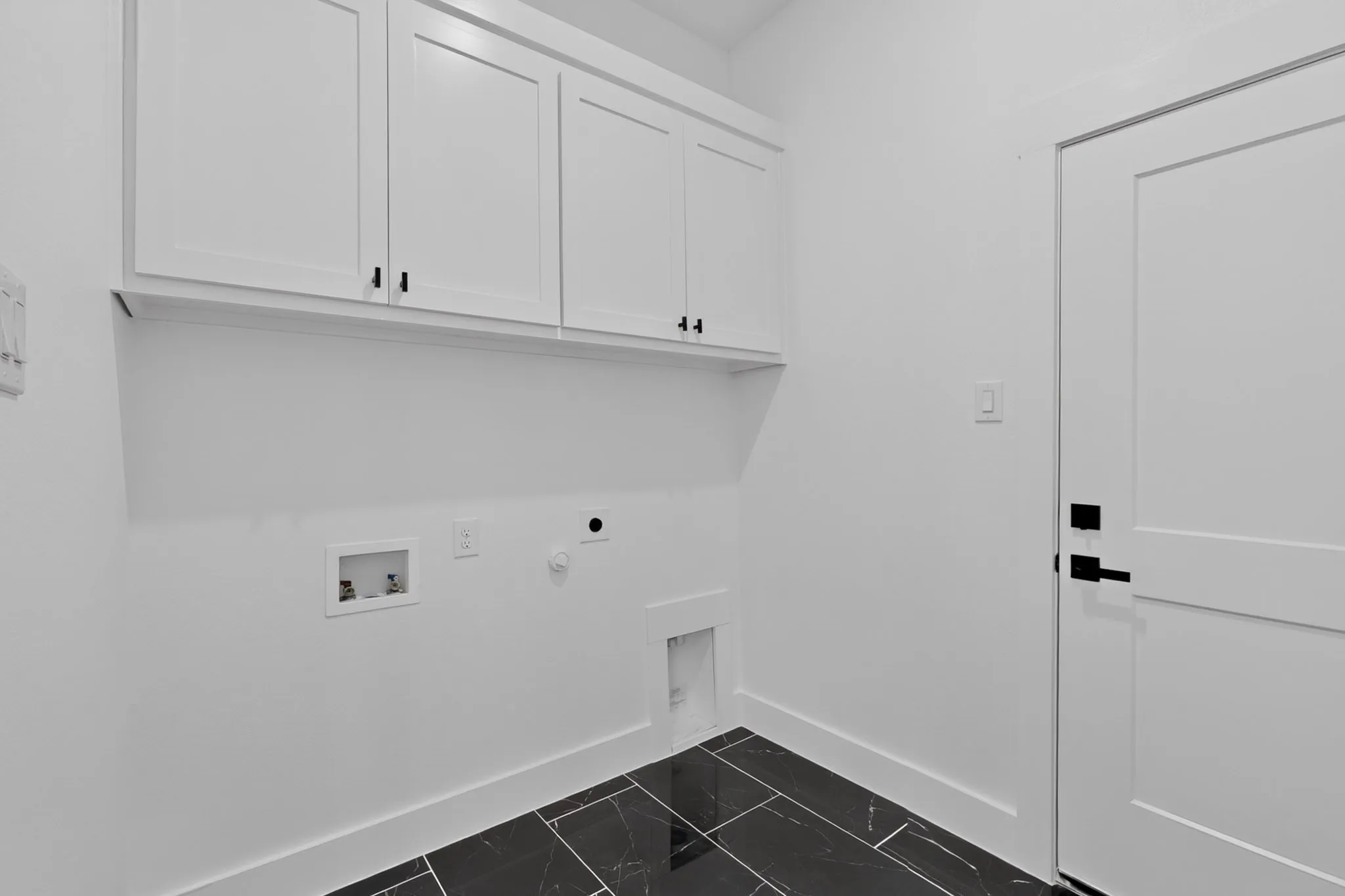 White shaker-style cabinetry with black hardware, black tile flooring, and white interior door with black hardware