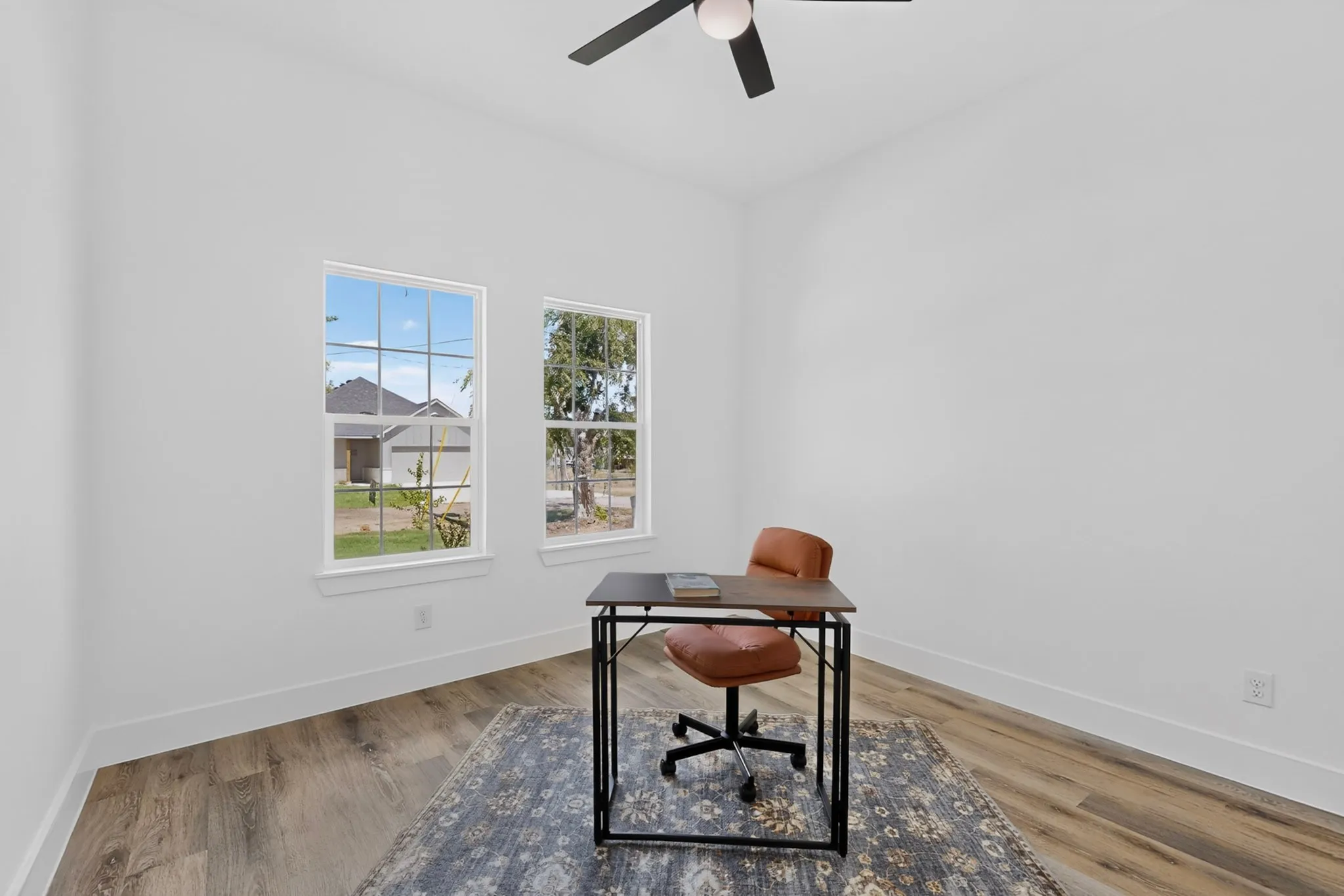 Bright interior featuring two windows, wood-finish flooring, a ceiling fan, and white walls
