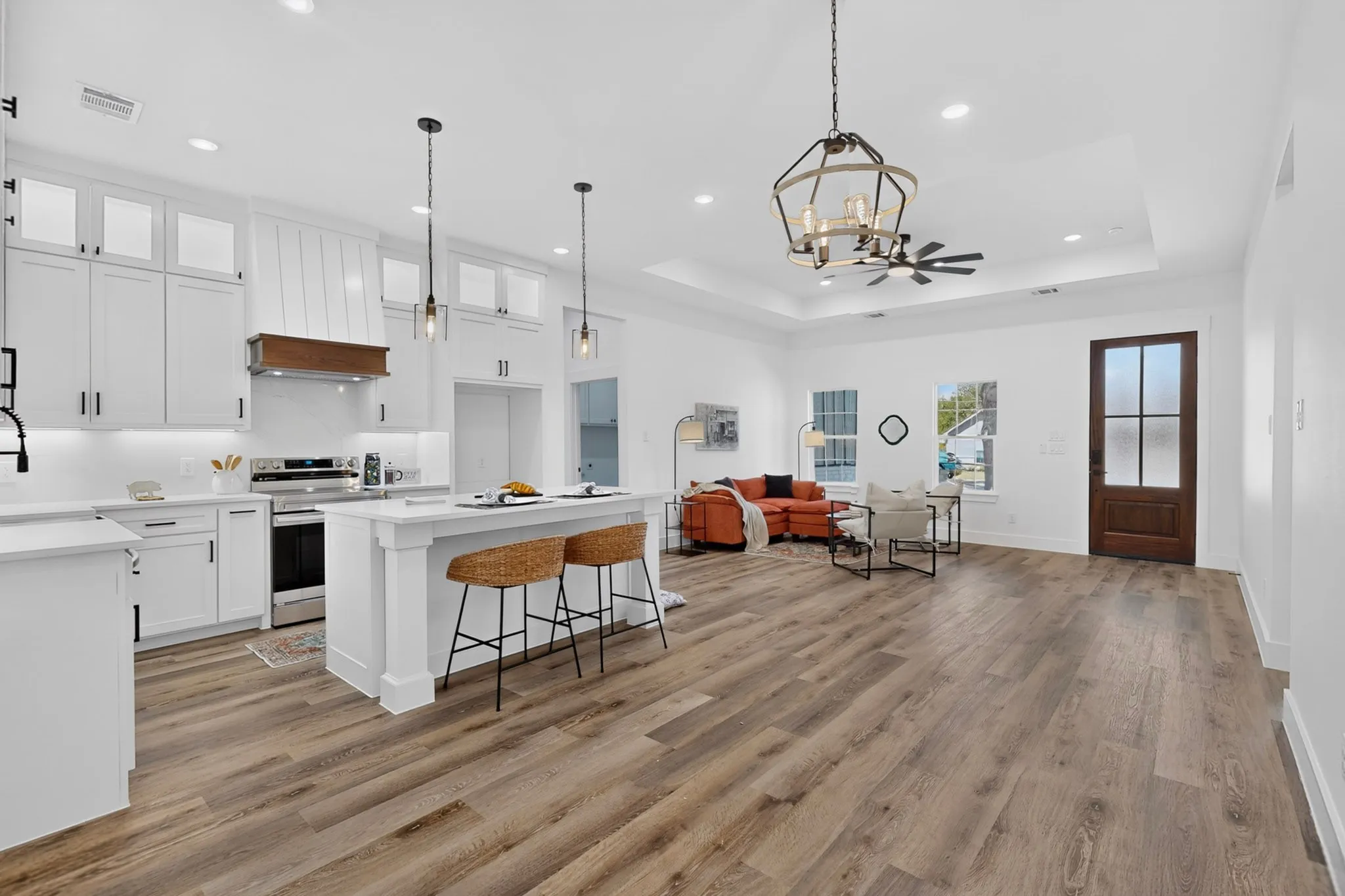 Open-concept kitchen and living area featuring wood-finish flooring, white cabinetry, a kitchen island, recessed lighting, and a tray ceiling