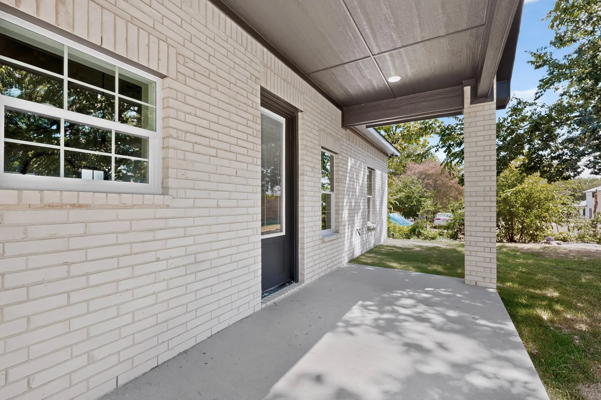 Covered porch with light-colored brick columns, concrete flooring, and recessed lighting