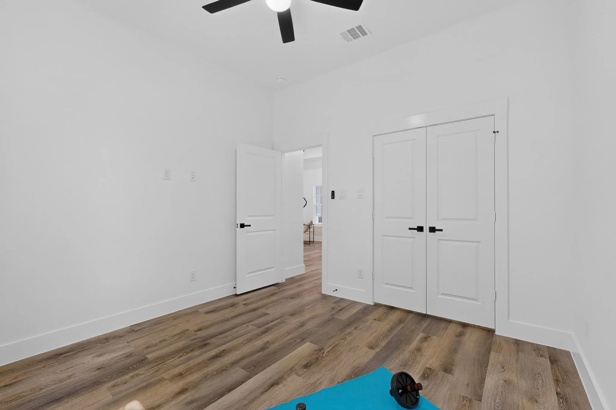 Wood-finish flooring, white walls, ceiling fan, white doors with black hardware, and an additional room entrance