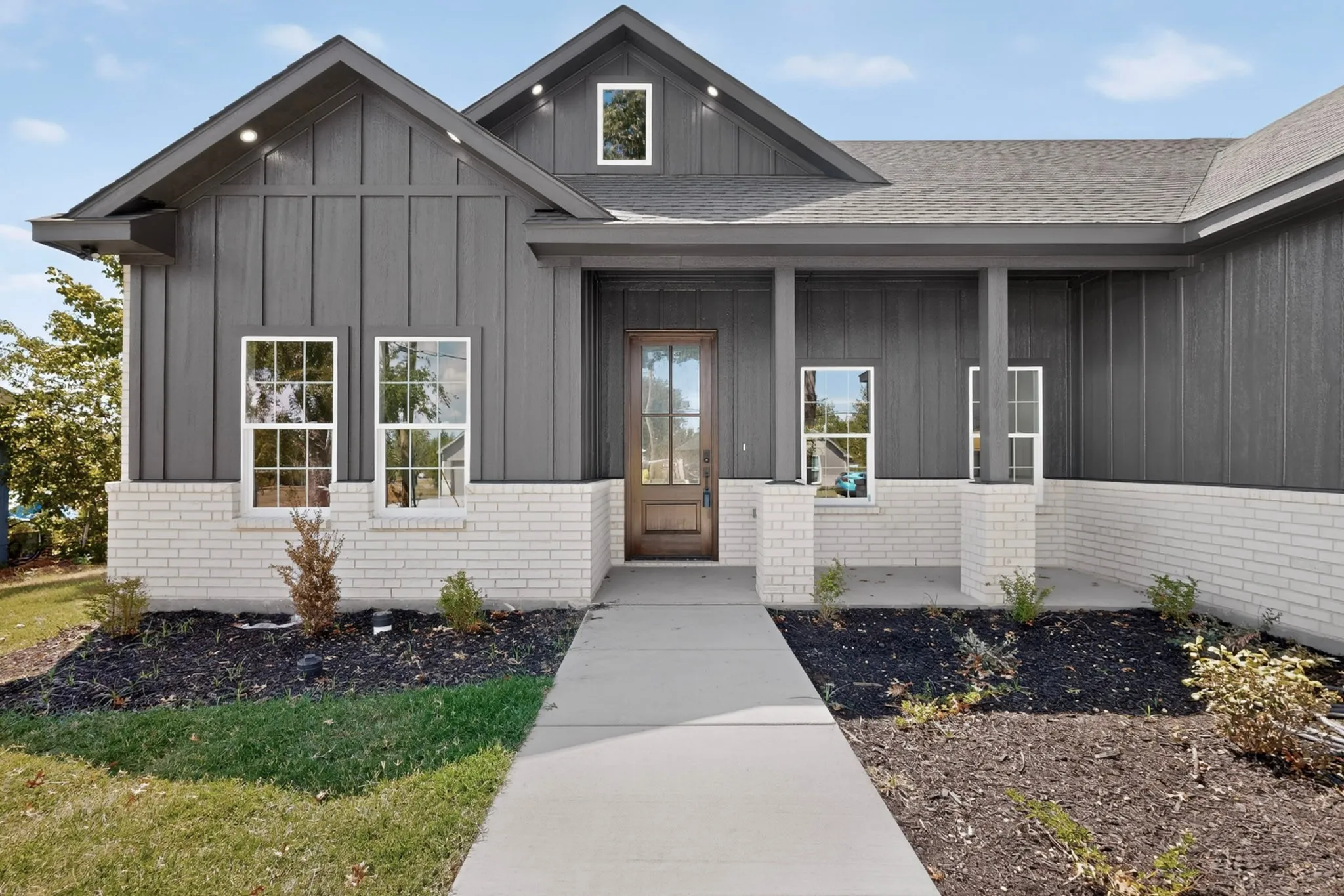 Exterior featuring dark vertical siding, white brick detailing, a covered porch entry, and a wood-panel front door with glass inserts