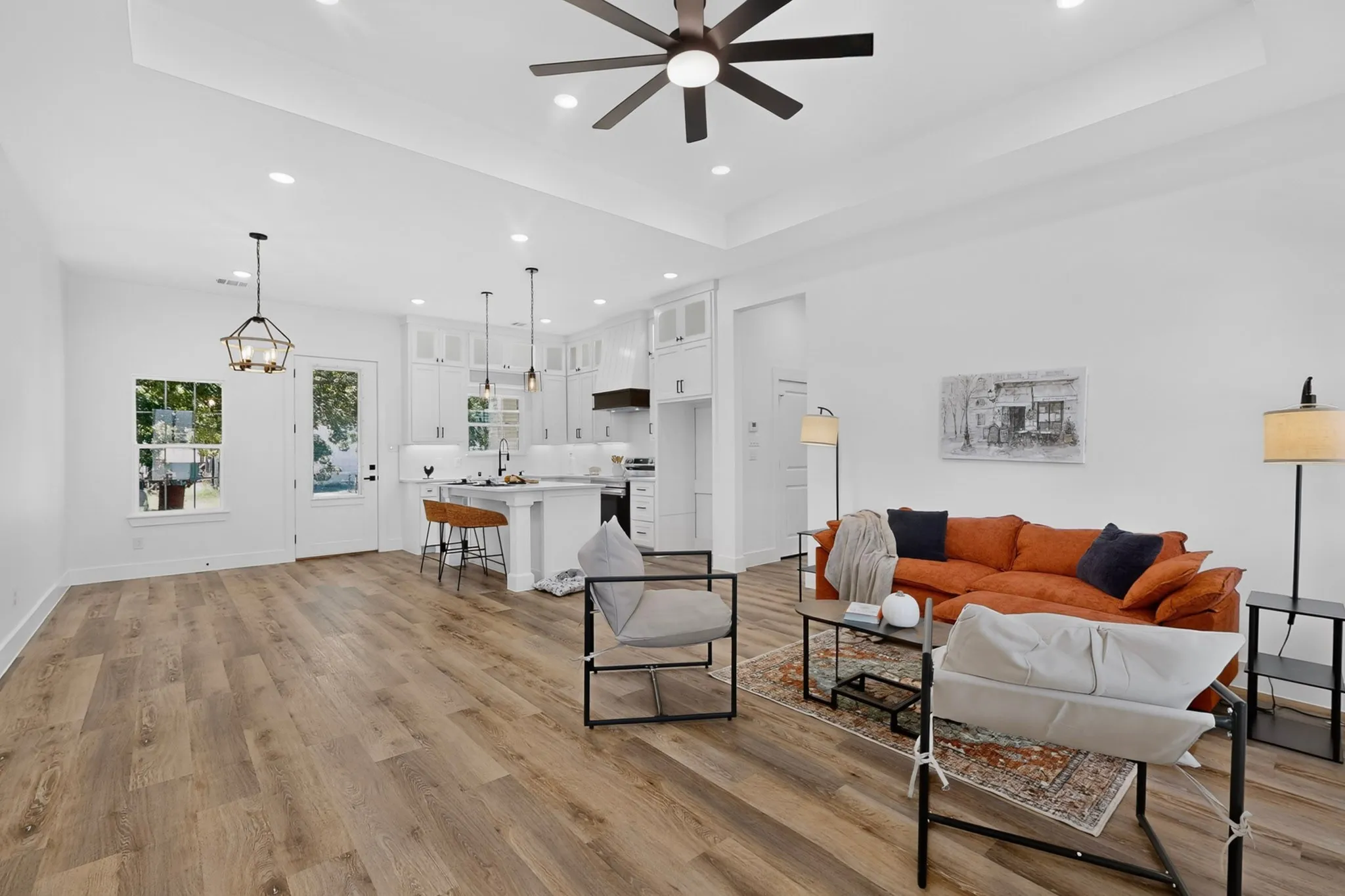 Open-concept living space featuring wood-finish flooring, a tray ceiling with recessed lighting, and a modern ceiling fan
