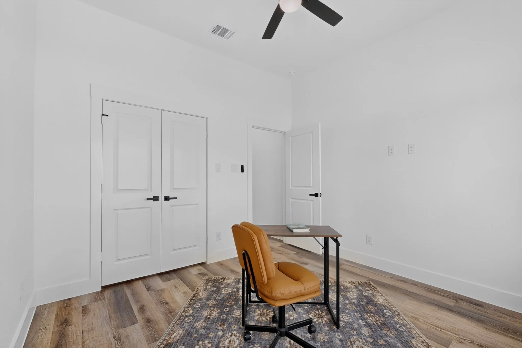 Interior room with wood-finish flooring, white walls, and a ceiling fan