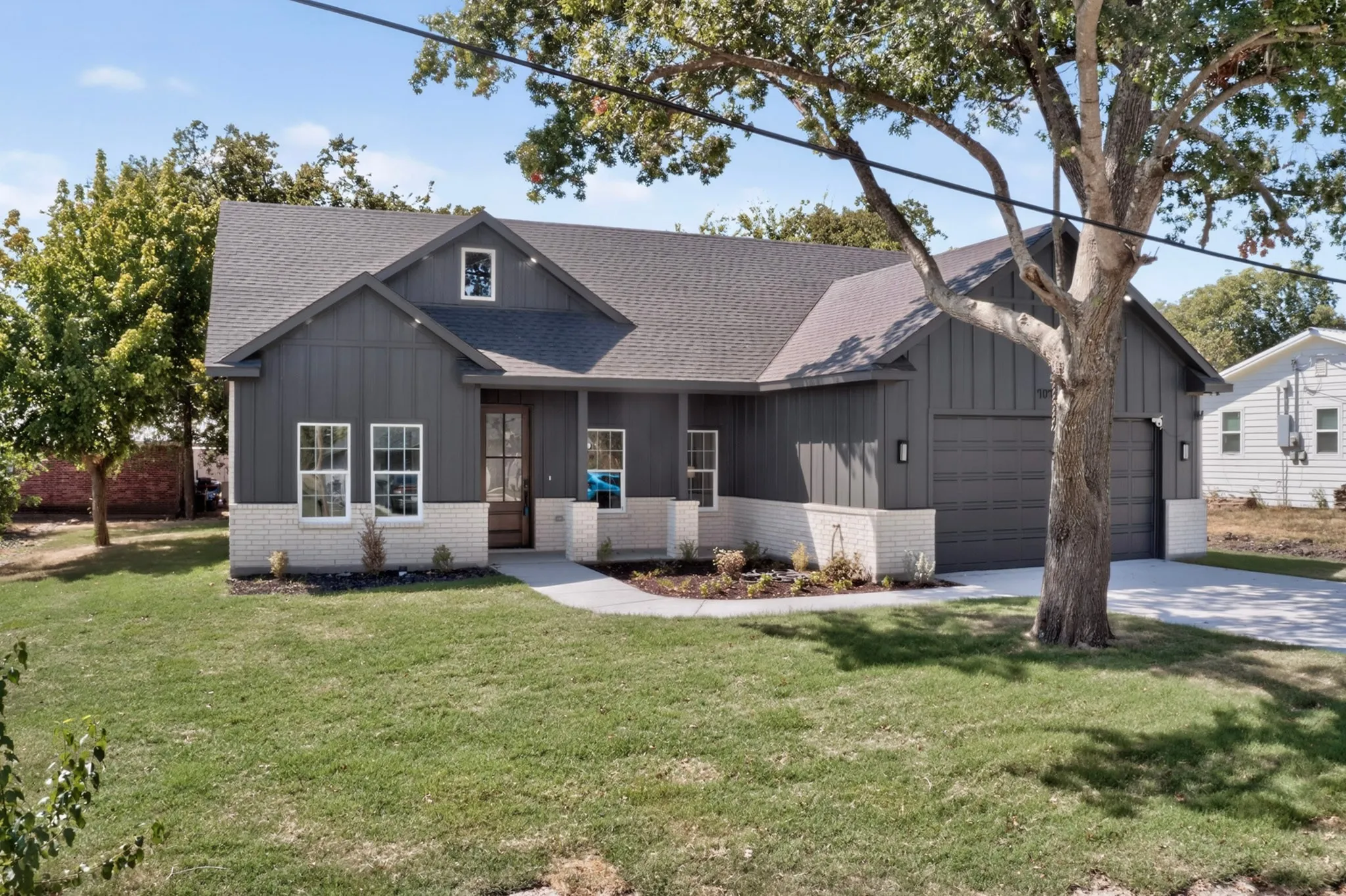 Board and batten siding with white brick accents, dark gray shingle roof, two-car garage, and a concrete pathway leading to the entry