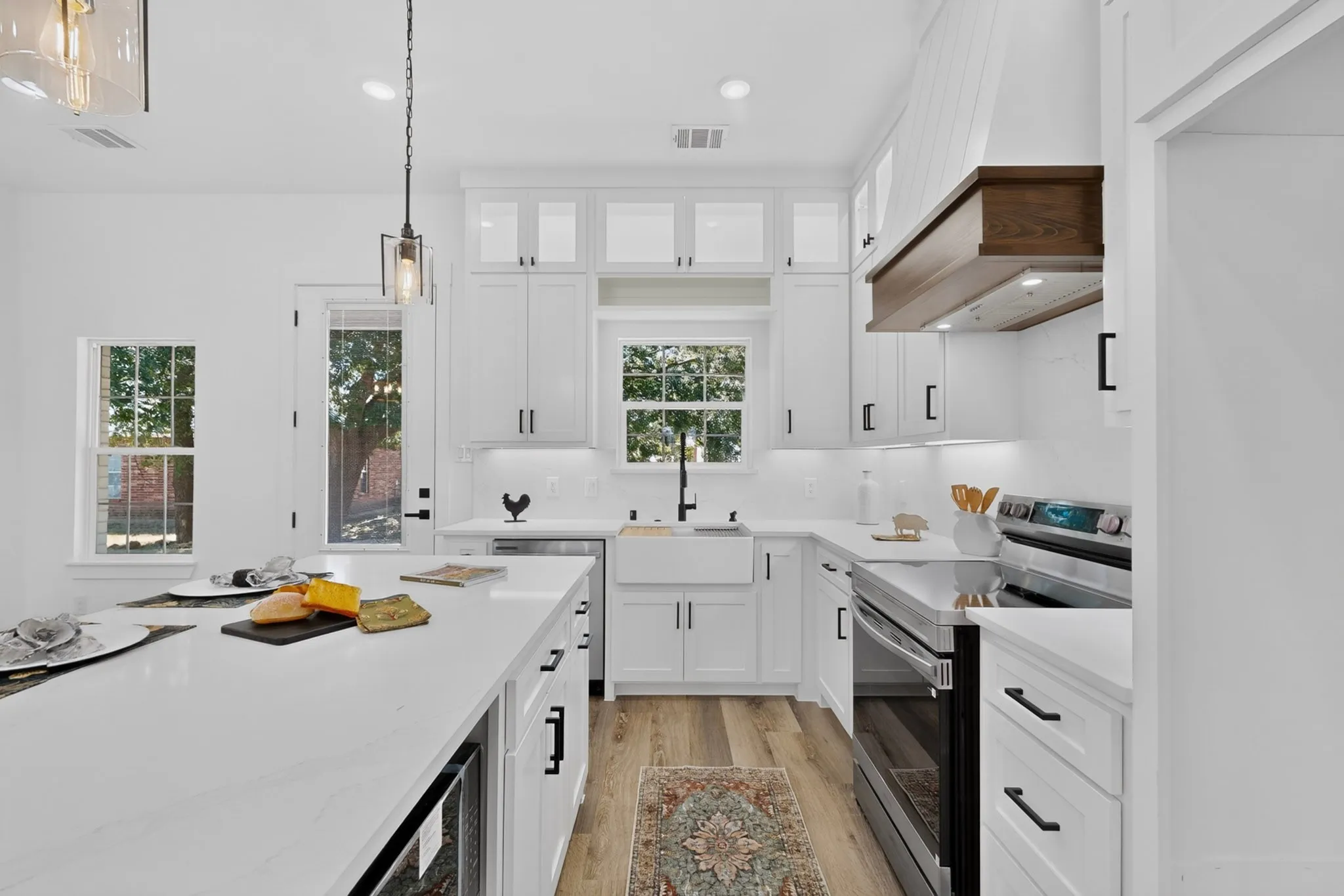 White kitchen featuring a large island, white cabinetry, integrated stainless steel appliances, and wood-finish flooring