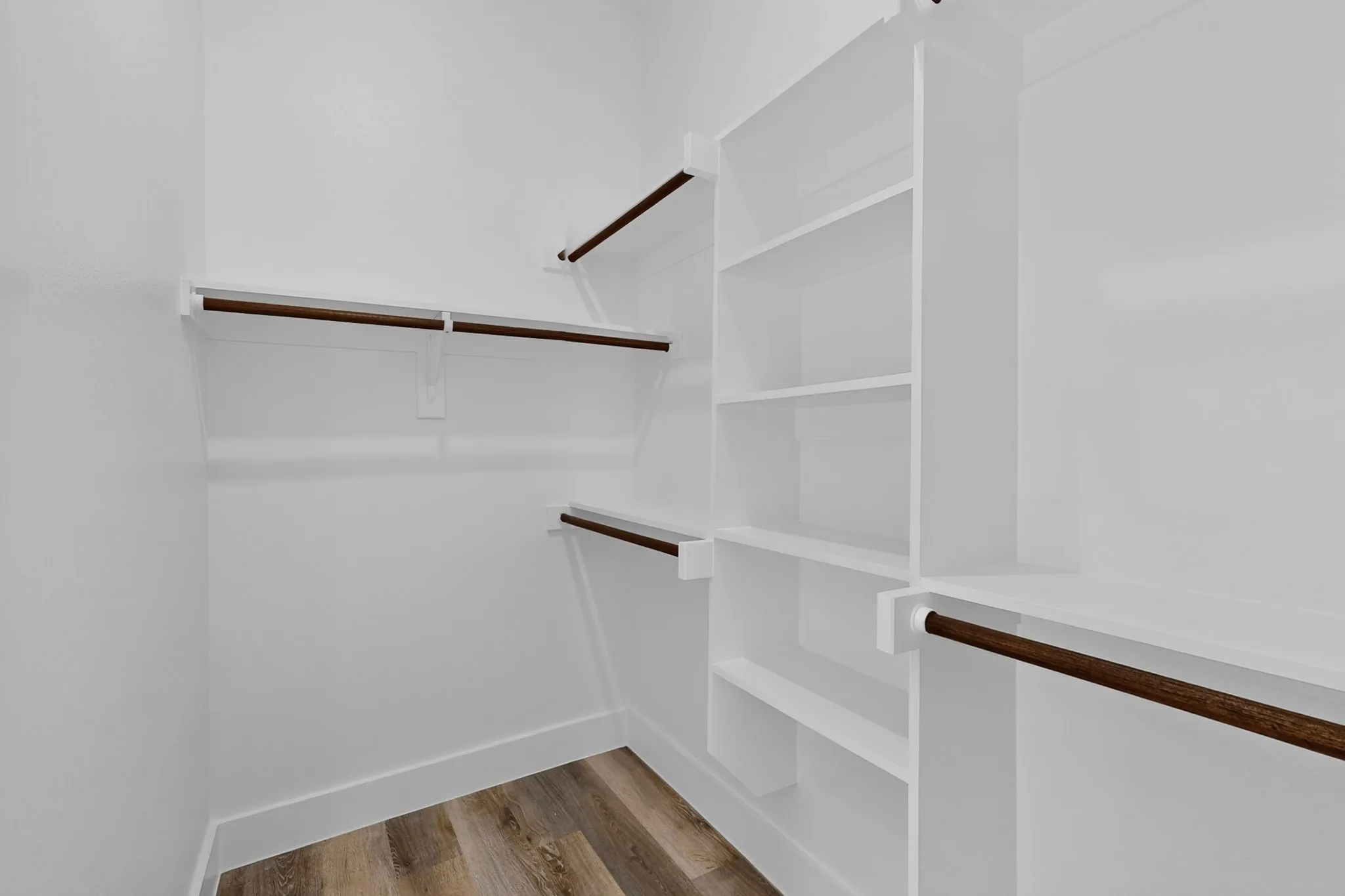 White shelving system, wood-finish flooring, white walls, and built-in hanging rods