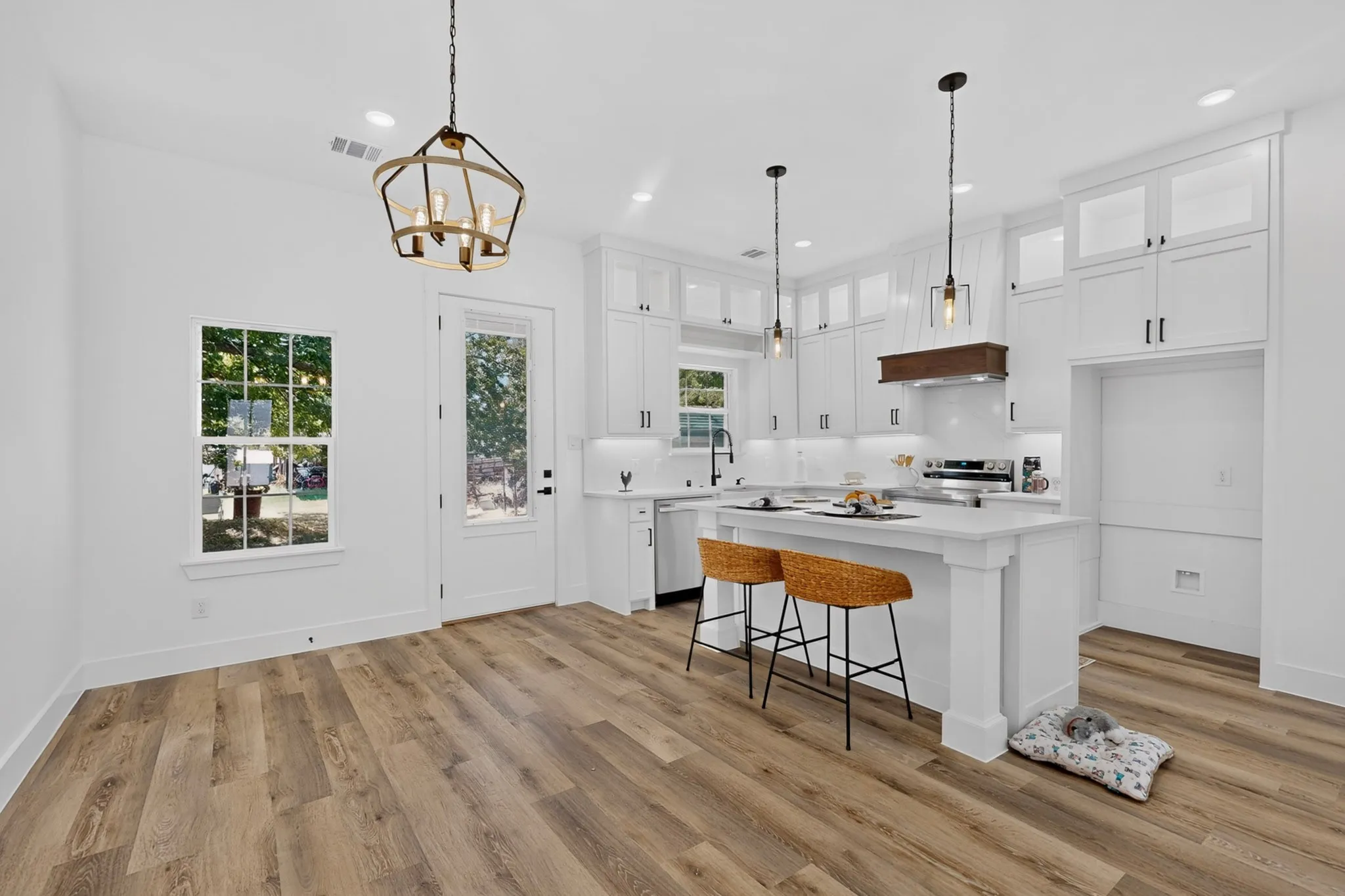 White shaker cabinetry, wood-finish flooring, central island with seating, pendant lighting, and stainless steel appliances