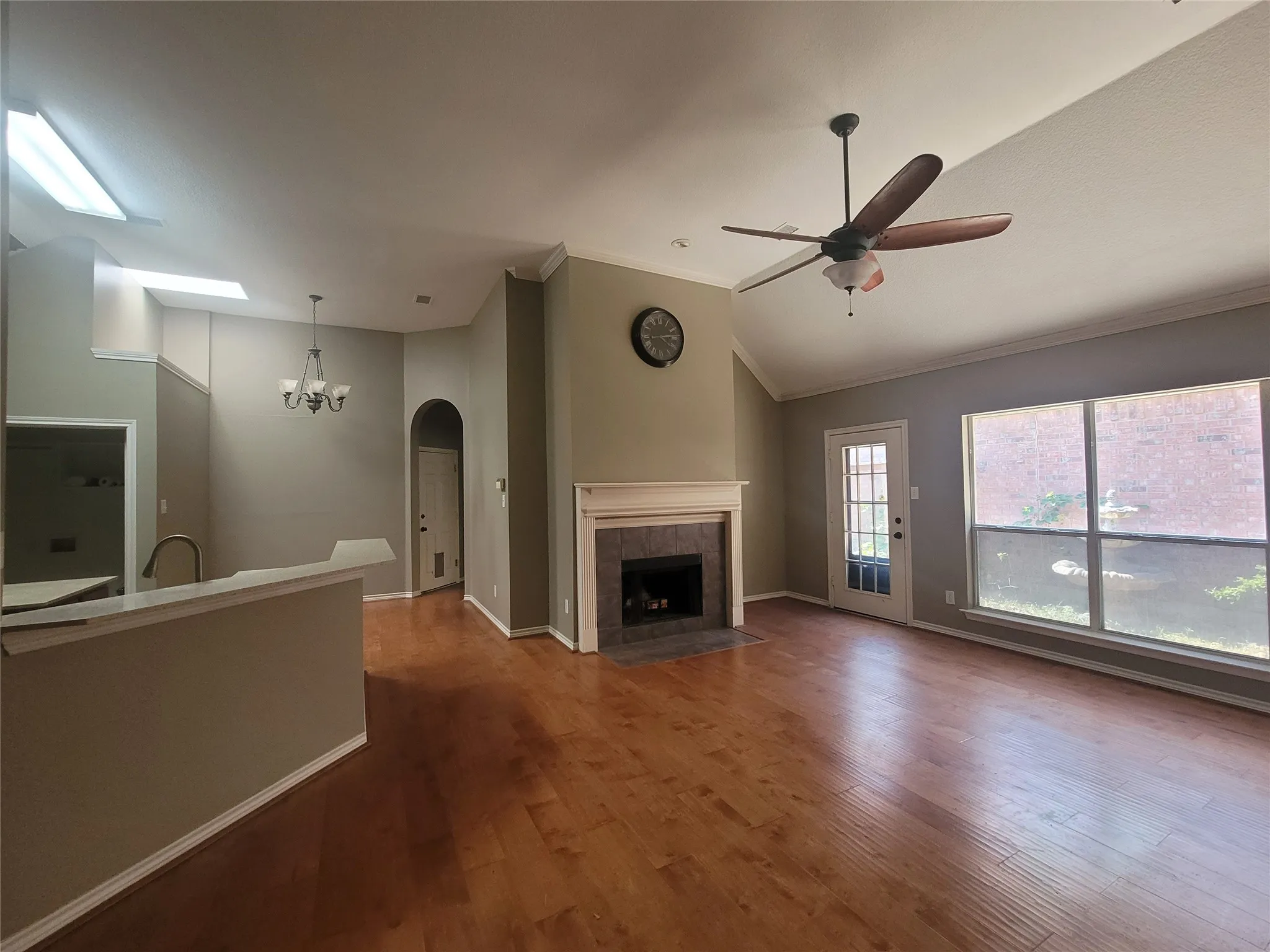 Vaulted ceiling, wood-finish flooring, fireplace with tile surround, built-in ceiling fan, and transom windows