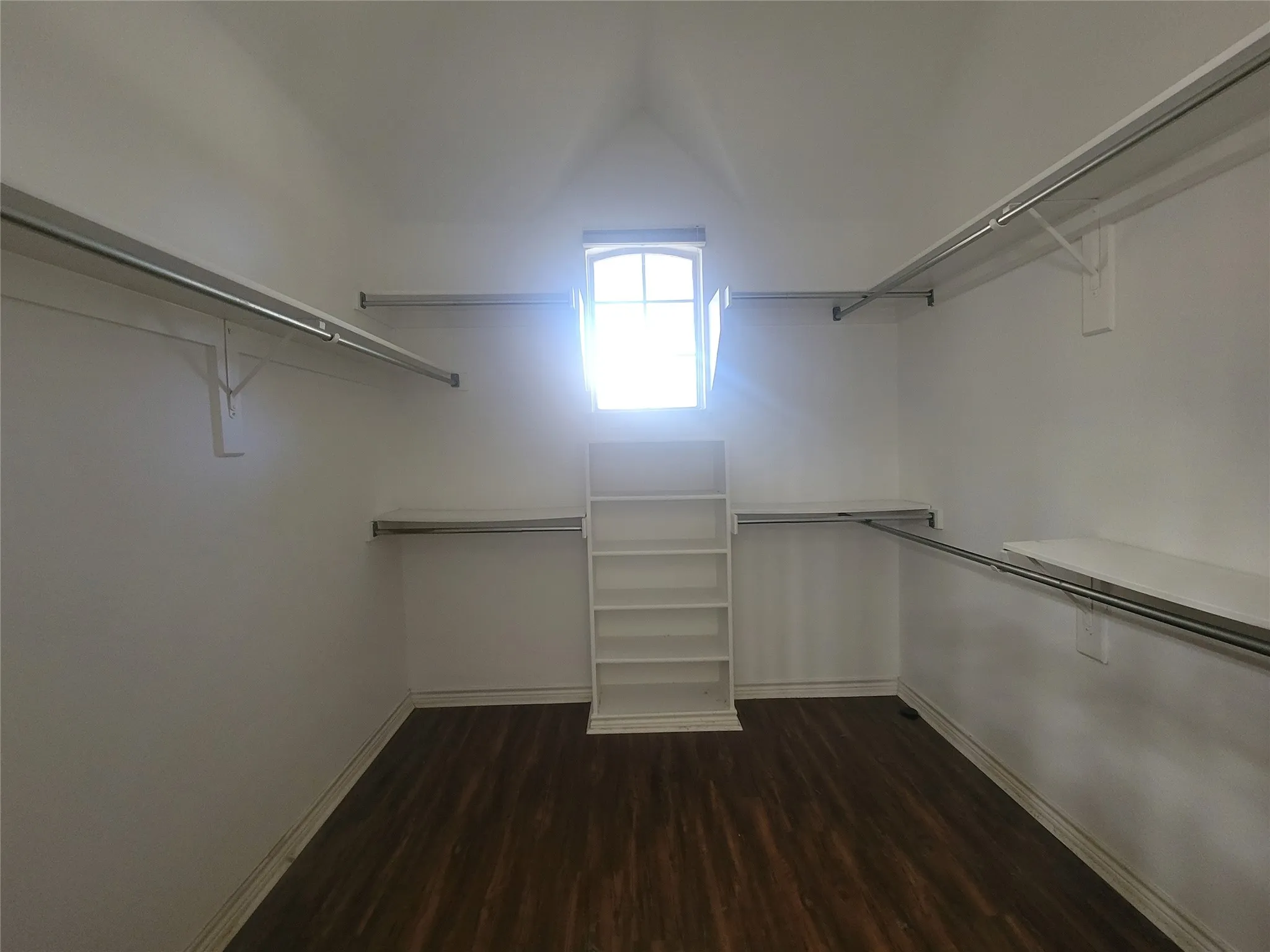 Walk-in closet featuring wood-finish flooring, a built-in shelving unit, and multiple hanging rods with shelving