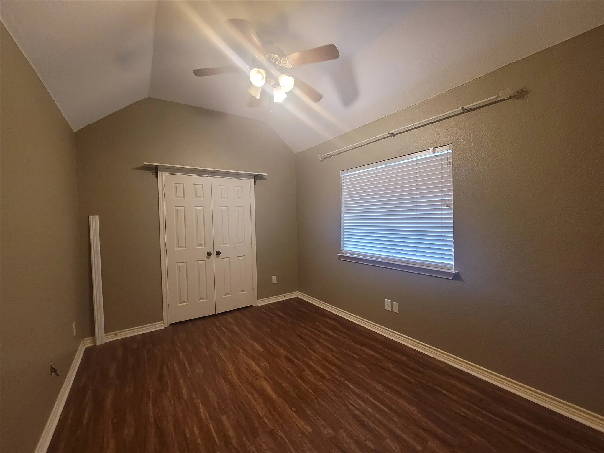 Vaulted ceiling, wood-finish flooring, ceiling fan, window with blinds, and bi-fold closet doors