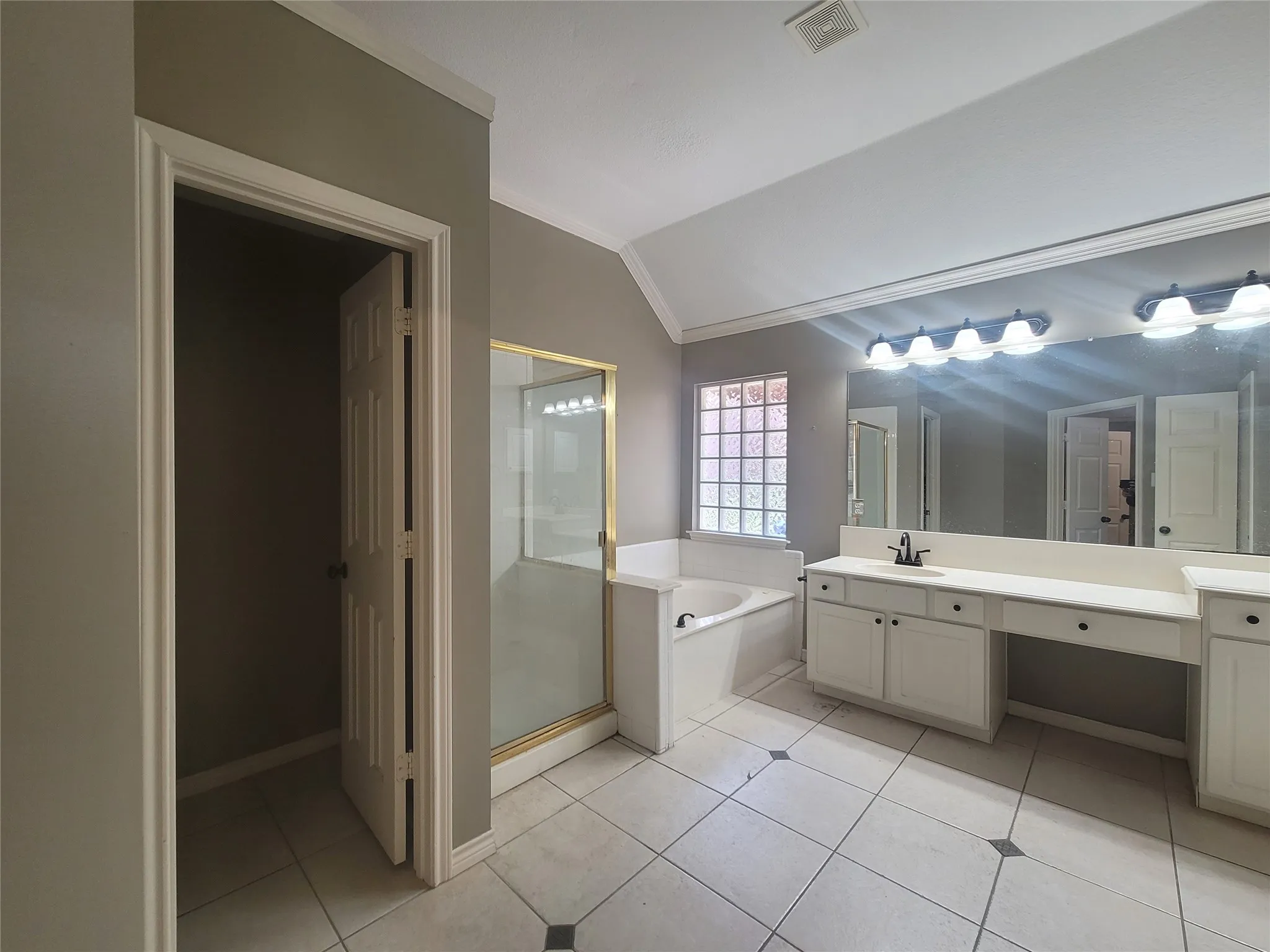 Spacious bathroom with vaulted ceiling, large vanity with dual sinks, built-in soaking tub, glass block window, and tiled flooring