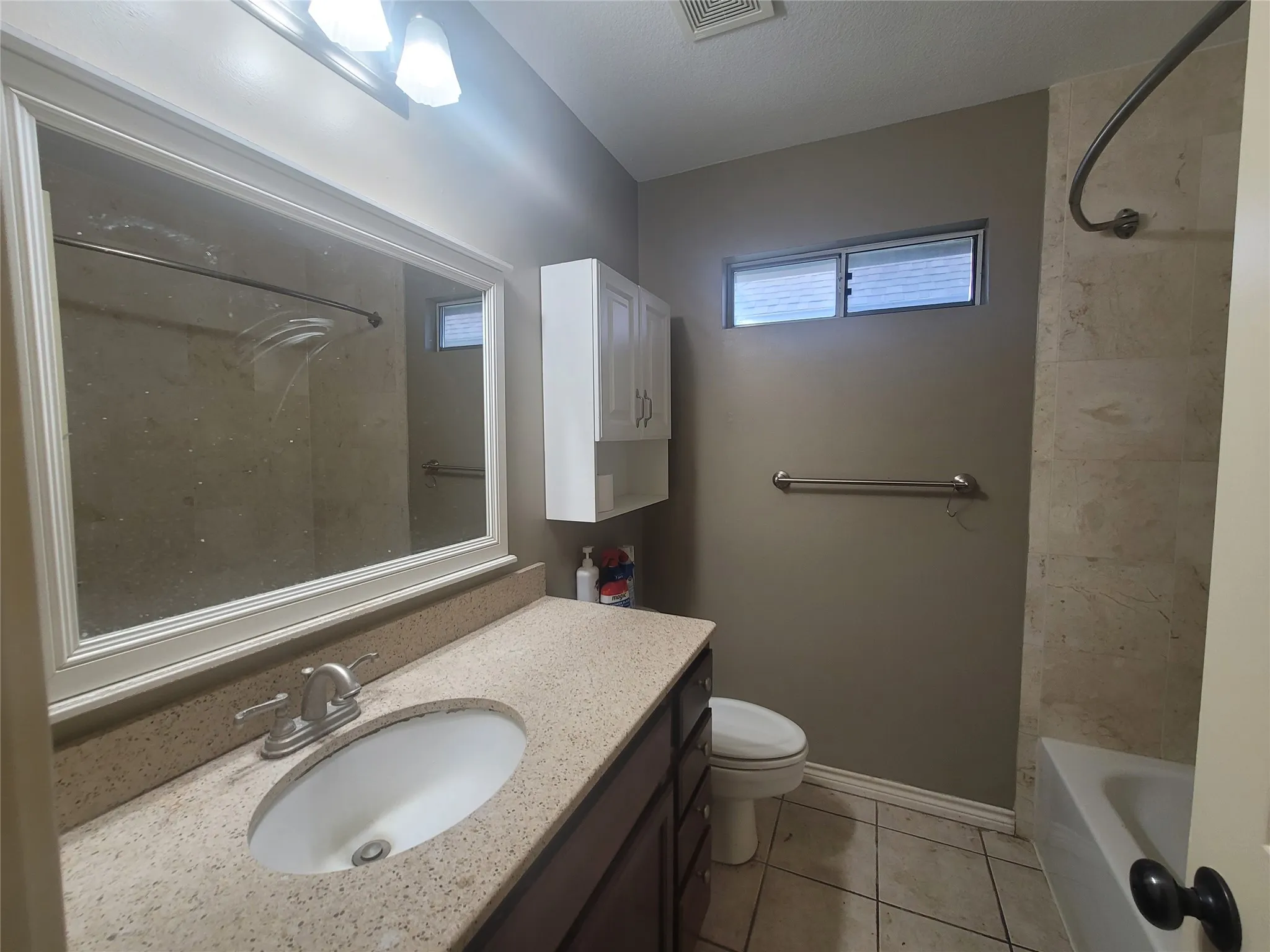 Bathroom featuring a vanity with an integrated sink, a large wall mirror, a tiled shower/tub combination, and a wall-mounted storage cabinet