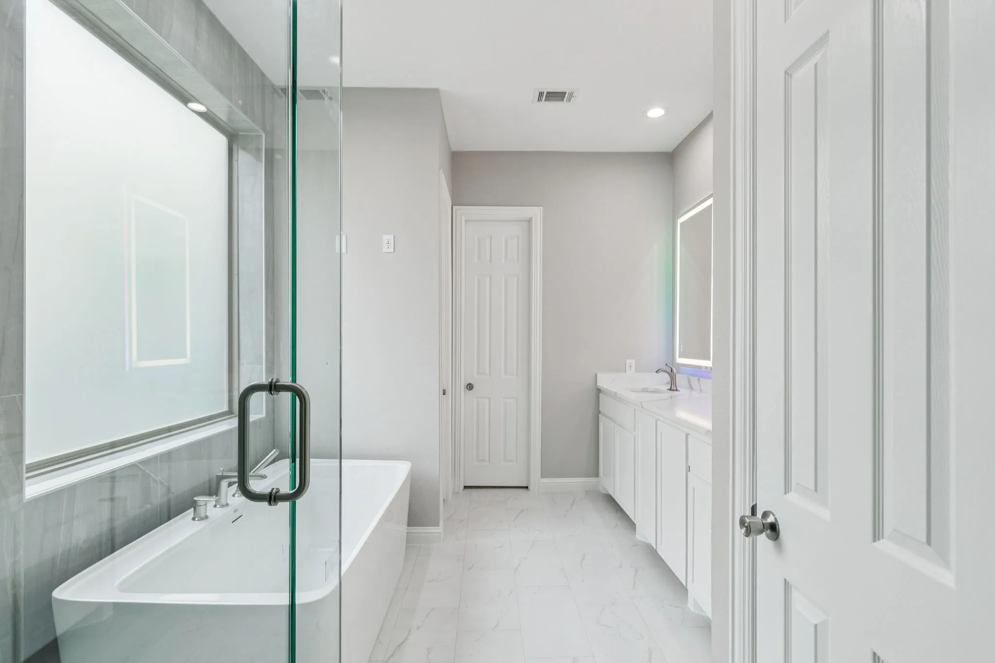 Freestanding tub with a glass shower enclosure, double vanity with white cabinetry, and recessed lighting