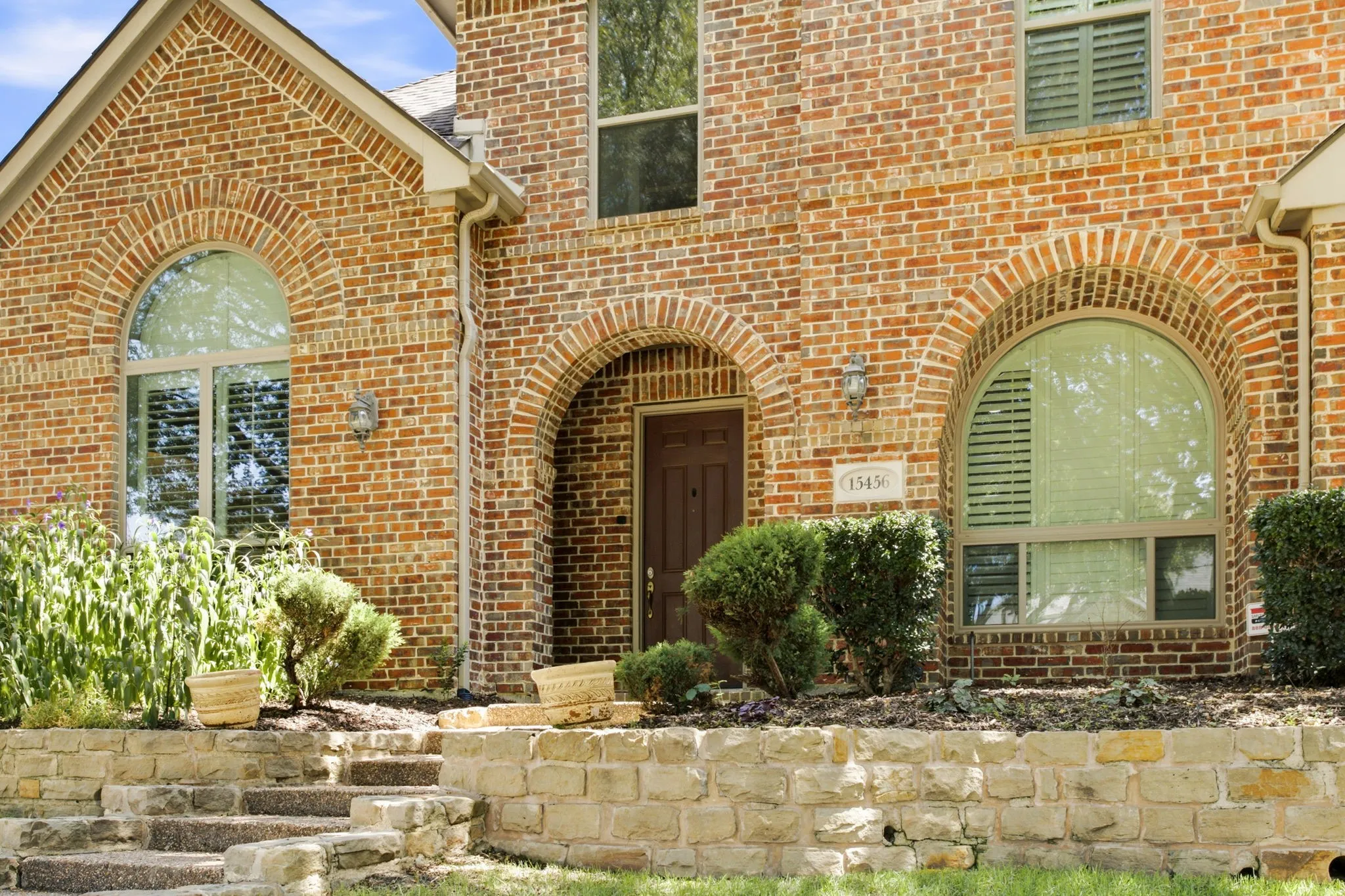Brick exterior with arched window details, stone retaining wall, and mature landscaping