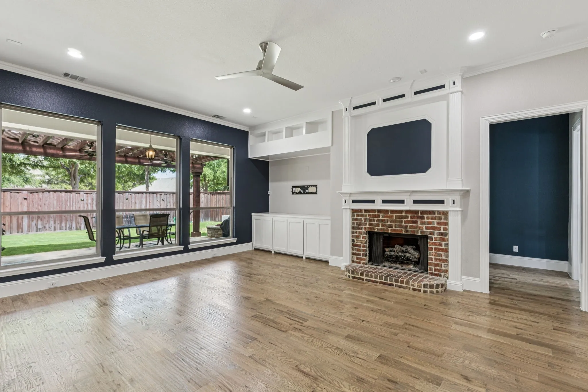 Wood-finish flooring, a brick fireplace with a white mantel, expansive windows, built-in cabinetry, and recessed lighting