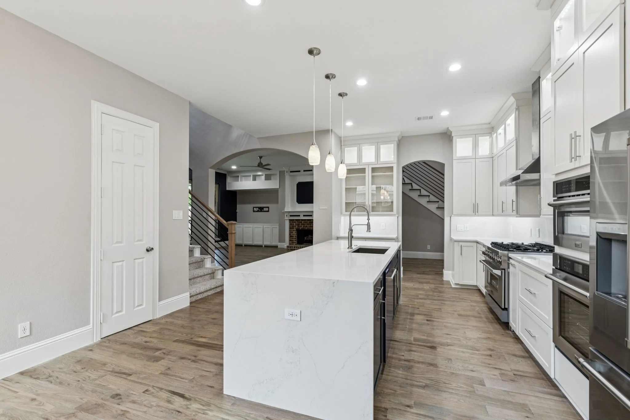 Gourmet kitchen featuring a large central island with sink, stainless steel appliances, white cabinetry with glass-front uppers, and wood-finish flooring