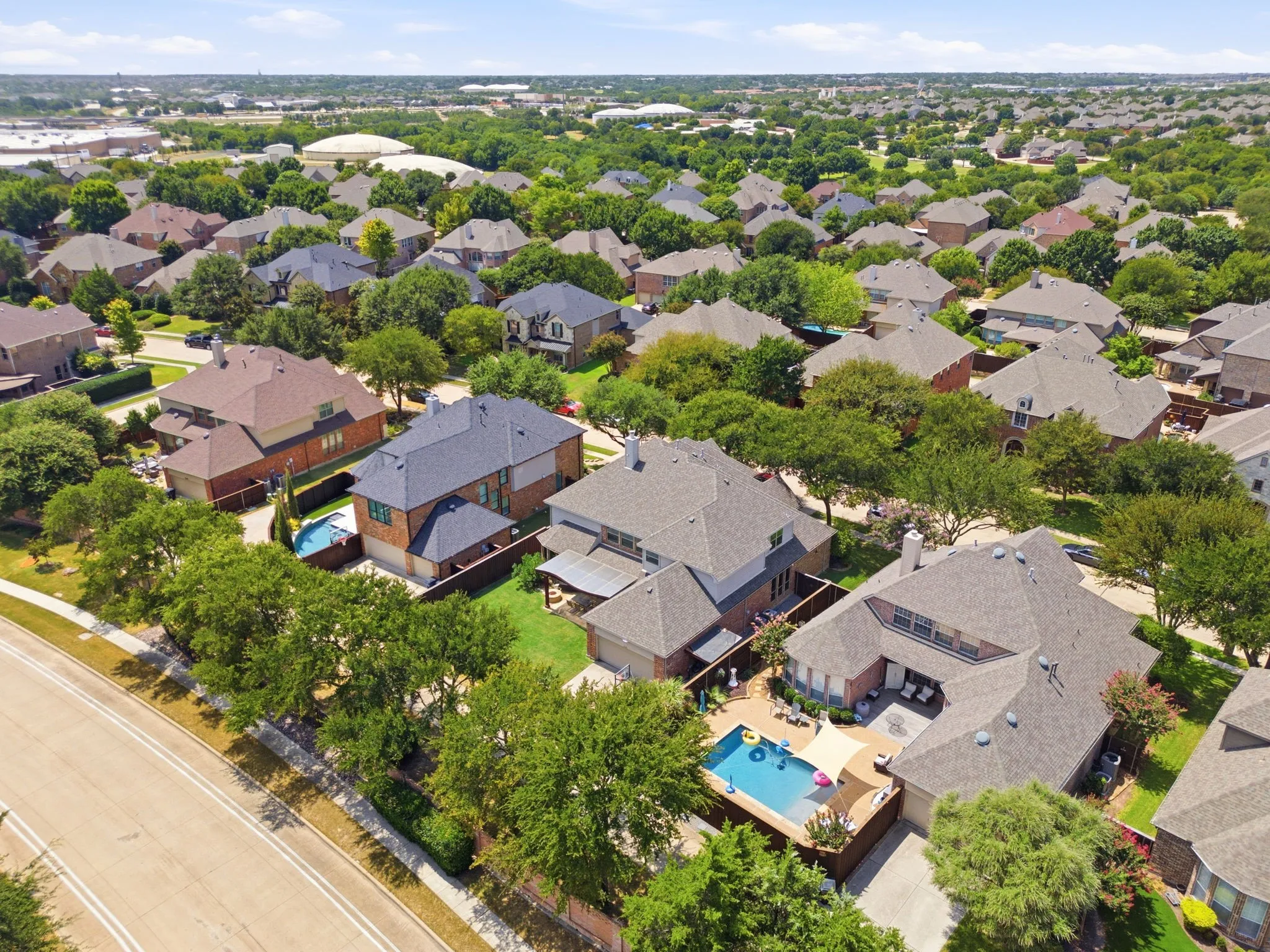 Aerial perspective showcasing a residential neighborhood with numerous detached homes, mature tree coverage, and private swimming pools
