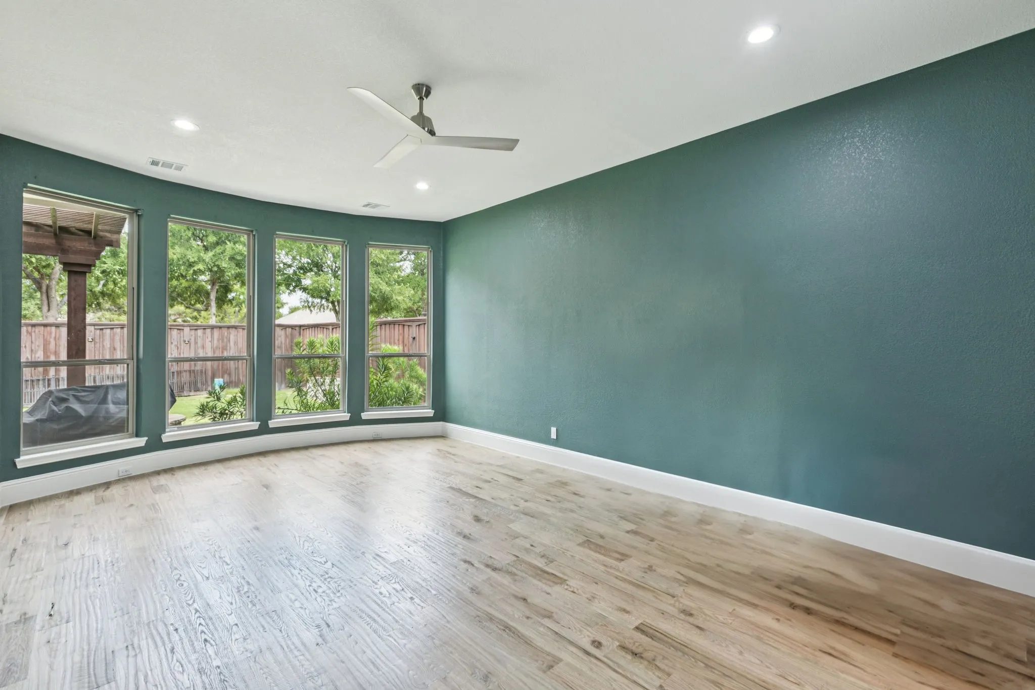 Curved wall with four large windows, wood-finish flooring, recessed lighting, and a ceiling fan