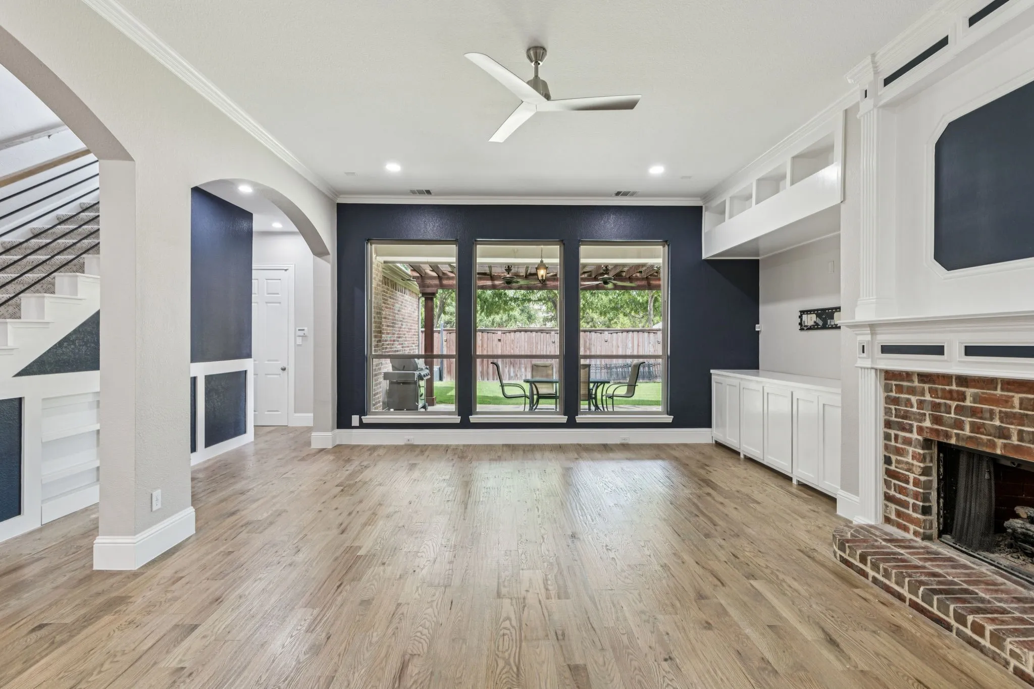 Expansive living area with wood-finish flooring, a traditional brick fireplace, and built-in cabinetry