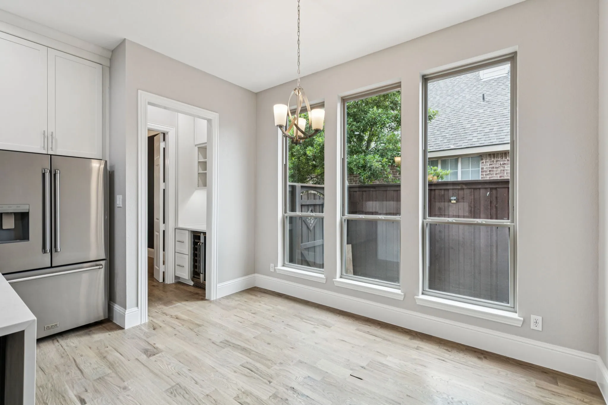 Wood-finish flooring, three large windows, stainless steel refrigerator, white cabinetry, and a contemporary chandelier