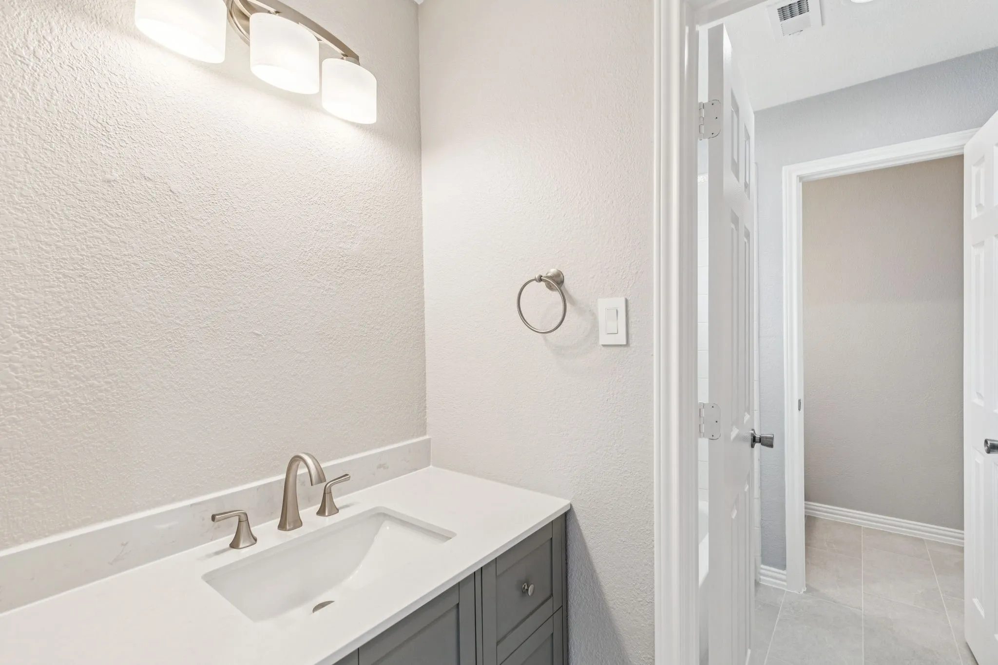 Vanity with integrated sink and brushed nickel faucet, light-toned countertop, and gray cabinetry