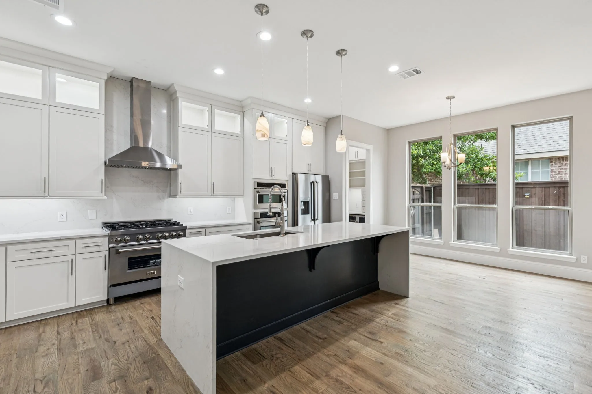 Gourmet kitchen featuring white shaker cabinetry, stainless steel appliances, a center island with a waterfall countertop, and wood-finish flooring