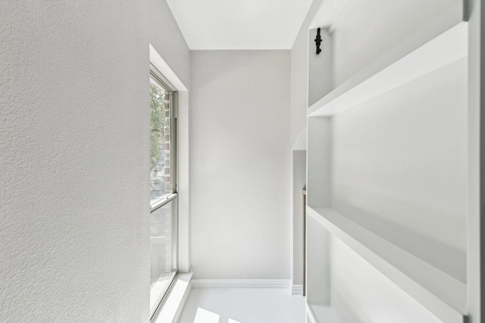 Built-in shelving, white walls, large window, and white trim