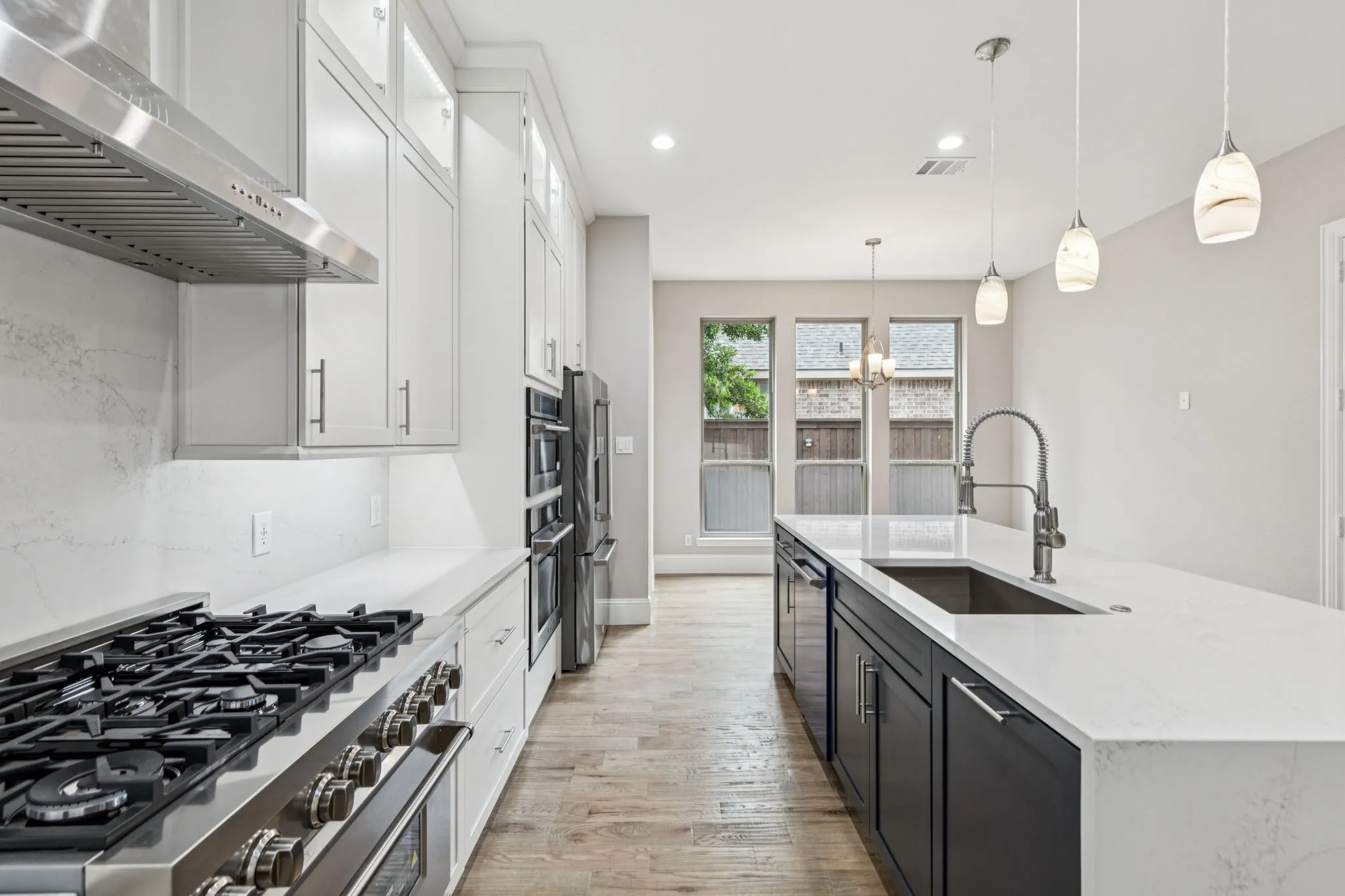 Gourmet kitchen featuring a gas range, stainless steel appliances, white cabinetry, a large island with sink, and wood-finish flooring