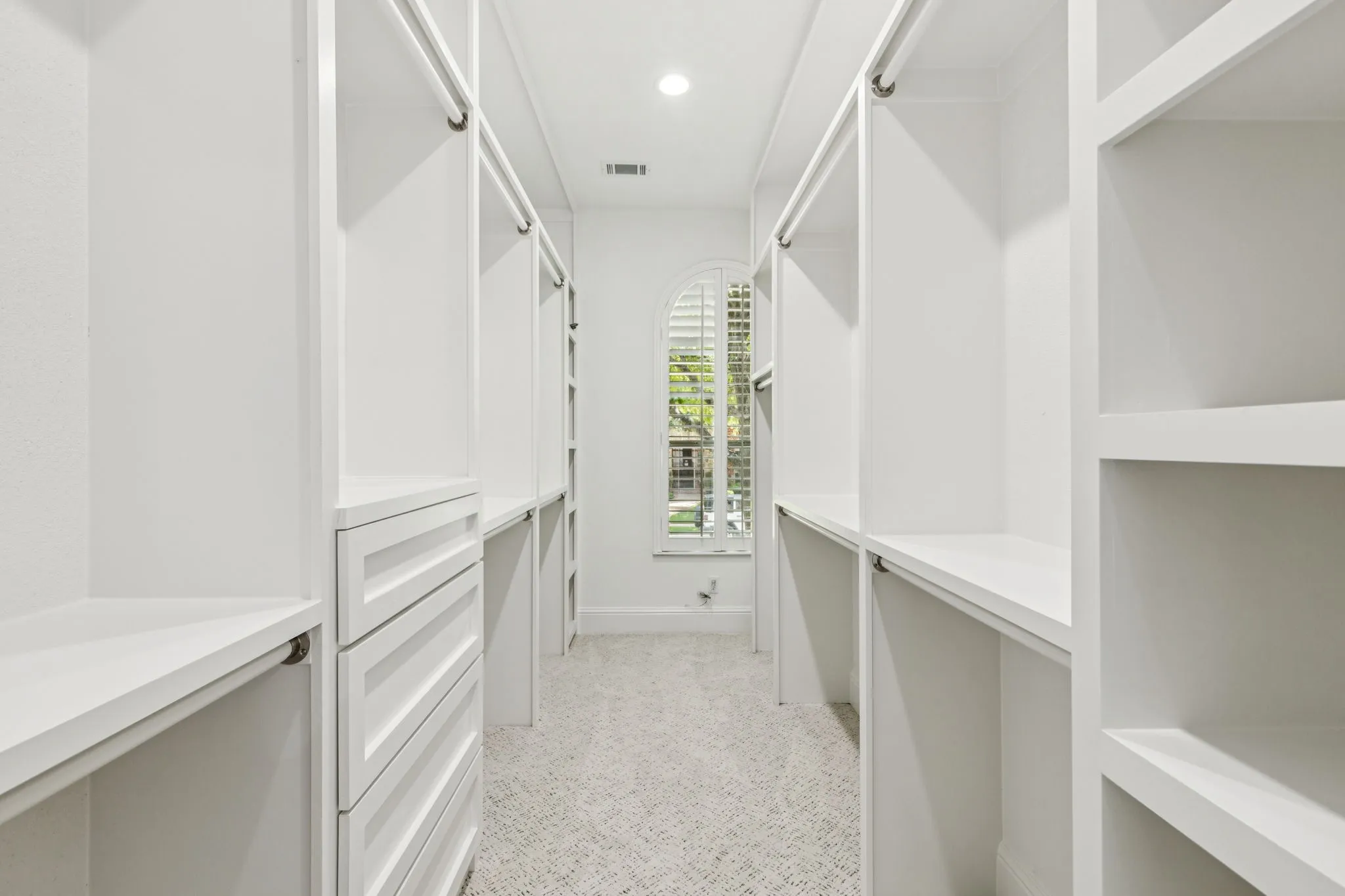 Walk-in closet featuring built-in shelving, hanging rods, integrated drawers, and an arched window with plantation shutters