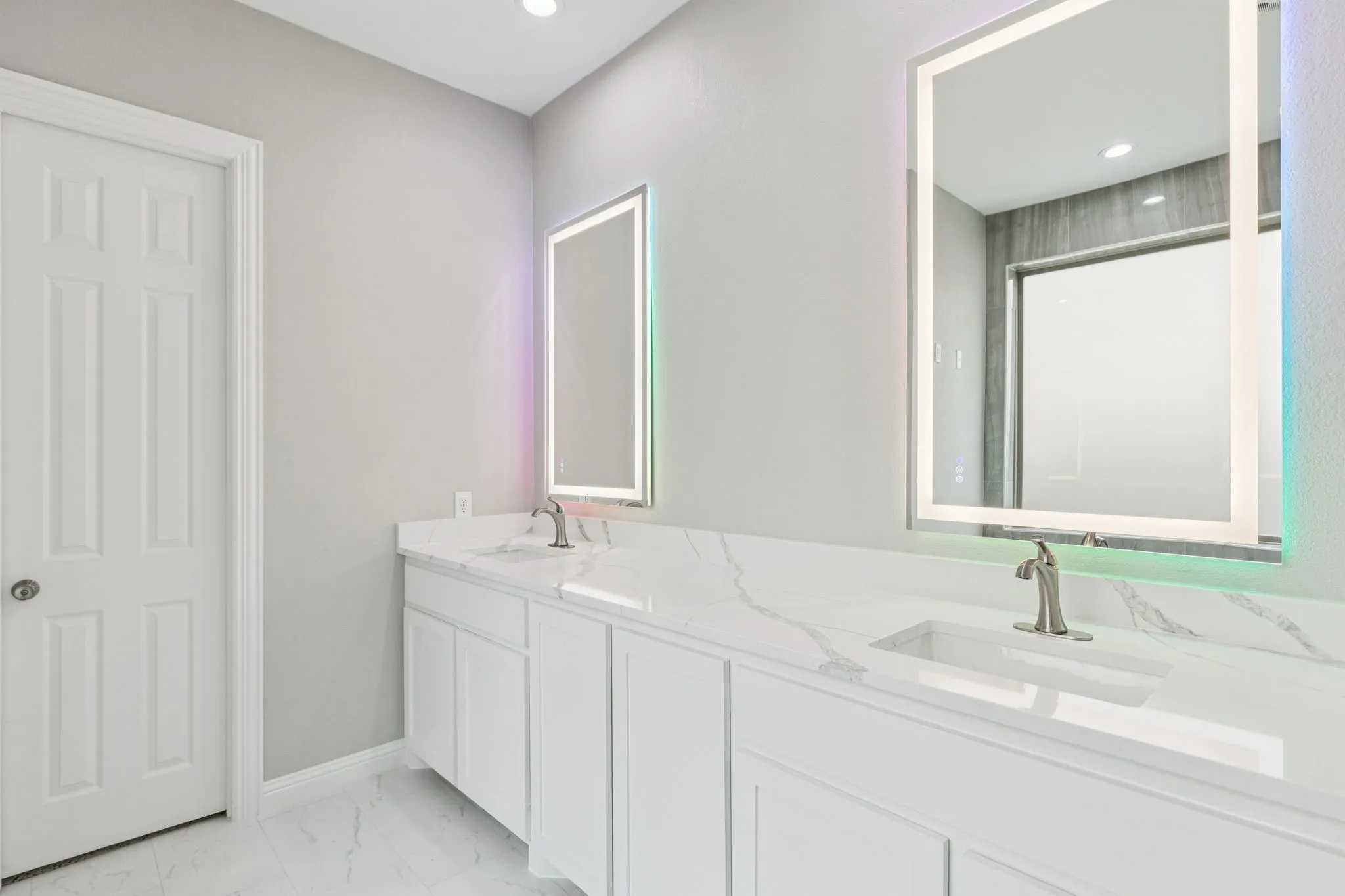 Dual vanities with integrated sinks, brushed nickel faucets, and back-lit mirrors