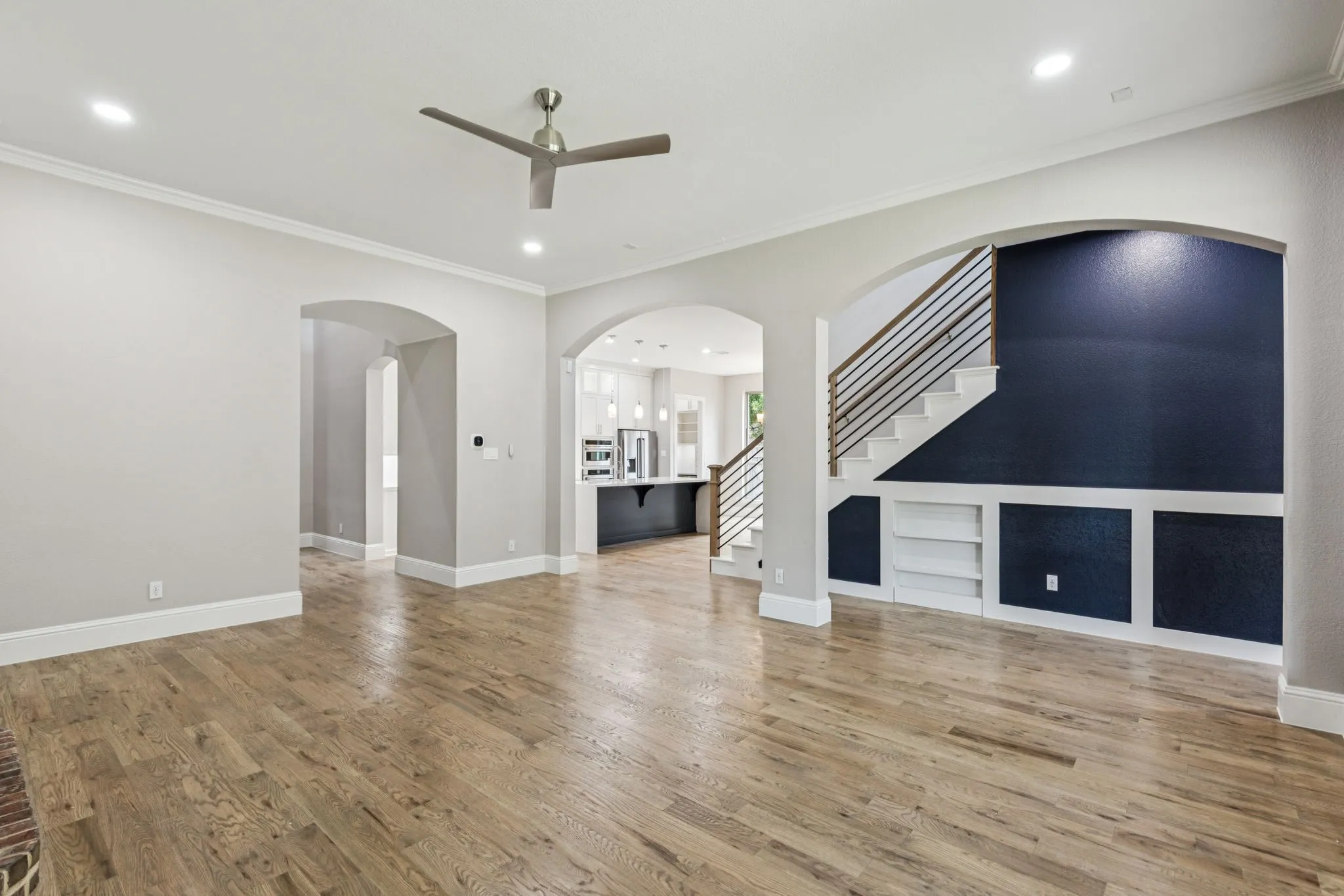 Wood-finish flooring, recessed lighting, ceiling fan, arched doorways, and built-in shelving