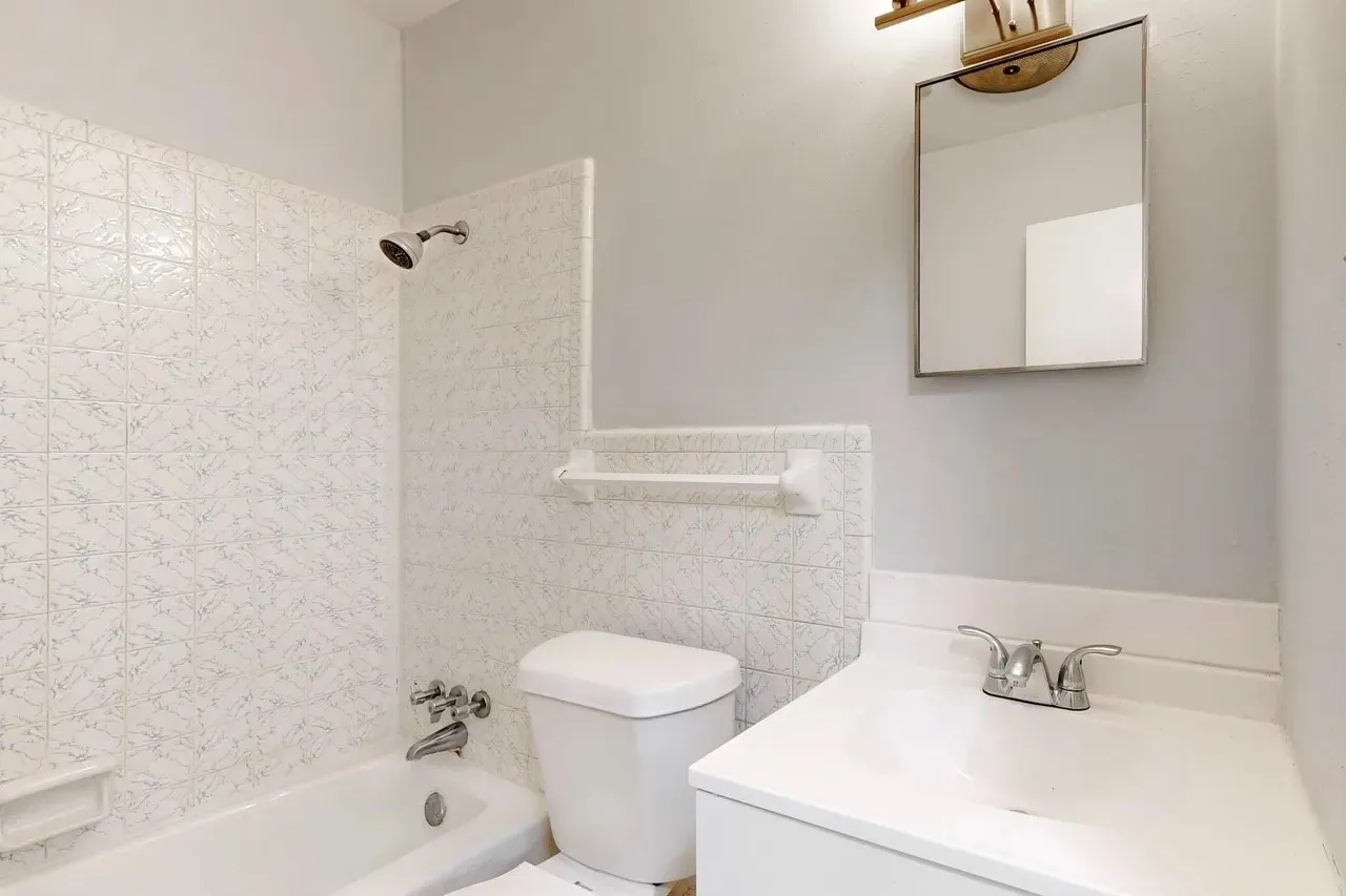 White bathtub with chrome fixtures, tiled shower surround, a toilet, a vanity with an integrated sink, and a mirrored medicine cabinet
