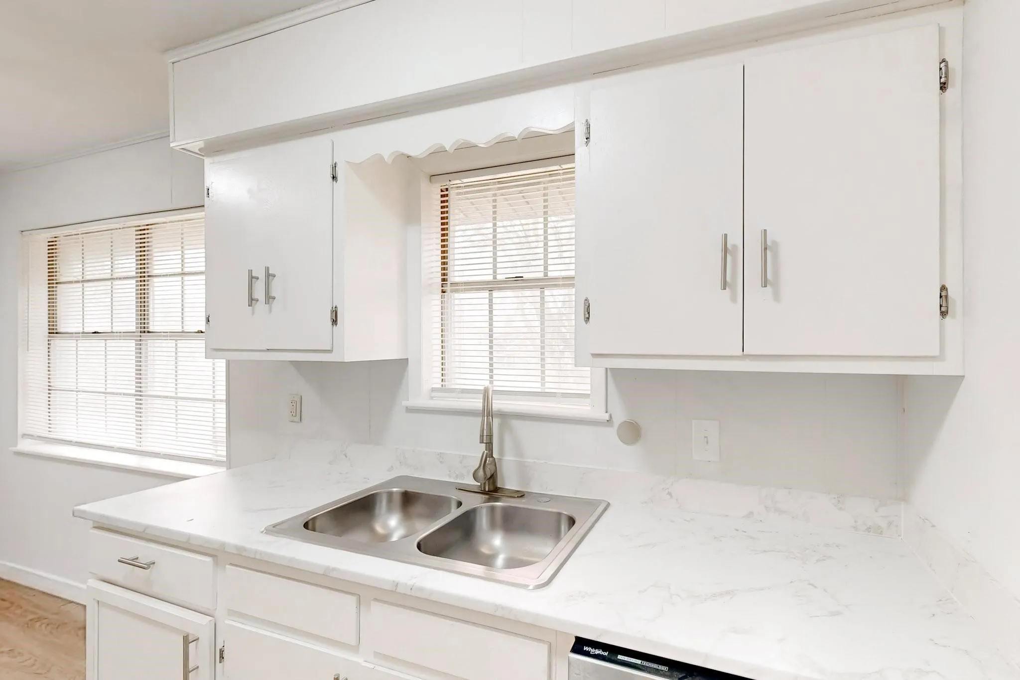 Kitchen featuring white cabinetry, a double basin stainless steel sink, and light-colored countertops