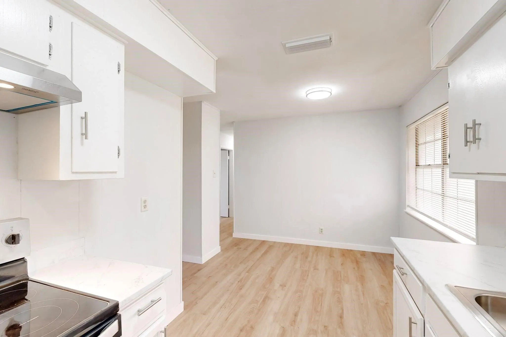 White cabinetry with brushed nickel hardware, light-toned wood-finish flooring, white countertops, and stainless steel range hood