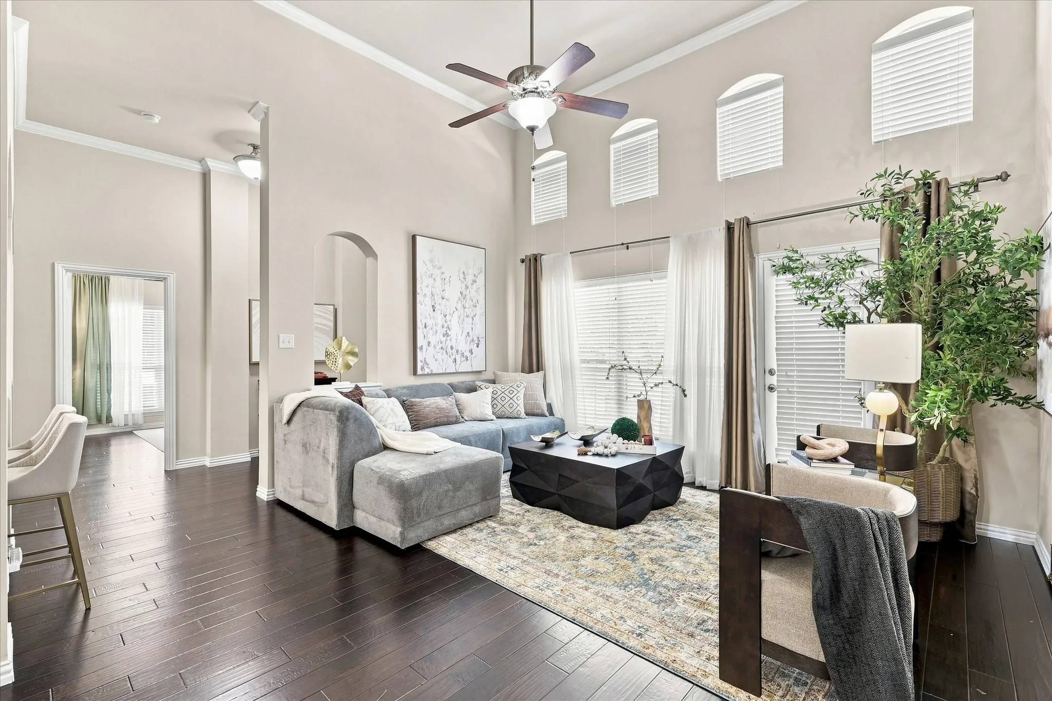 The bright, open living room features tall ceilings and a wall of windows, creating a spacious setting filled with natural light.