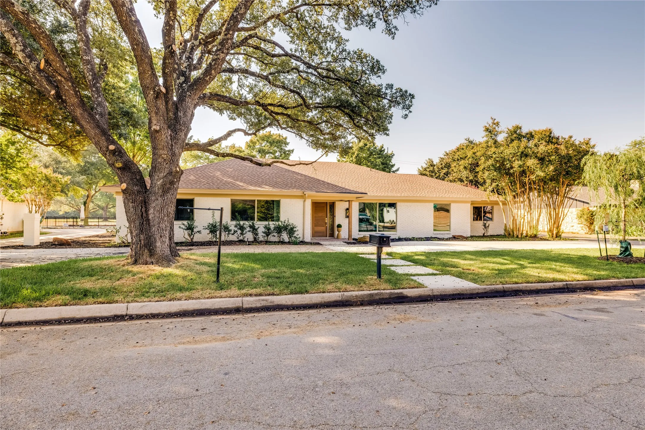 Ranch-style home with a prominent mature tree, light-colored exterior, and a brown shingle roof