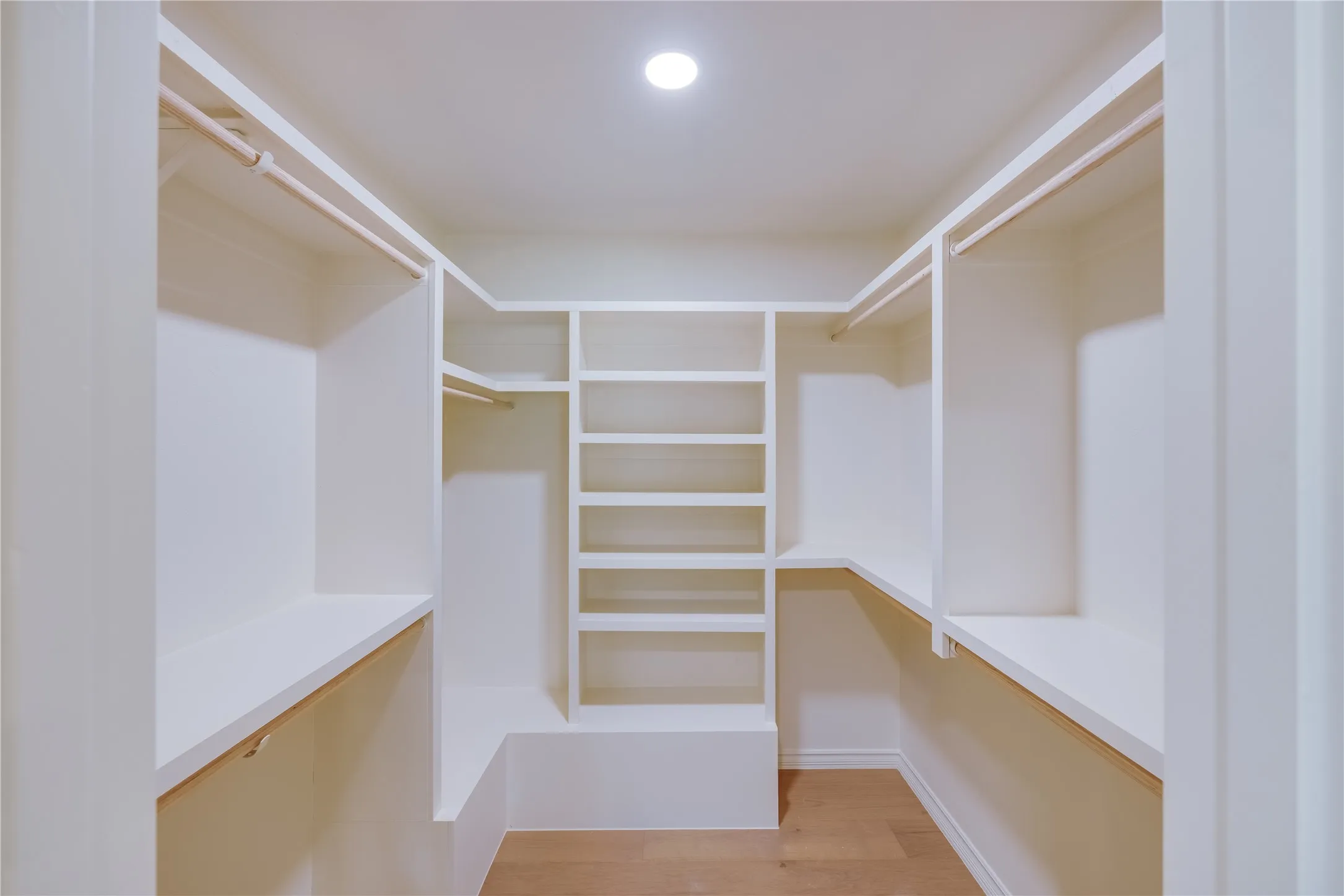 Walk-in closet featuring built-in shelving, multiple hanging rods, white-painted cabinetry, recessed lighting, and wood-finish flooring