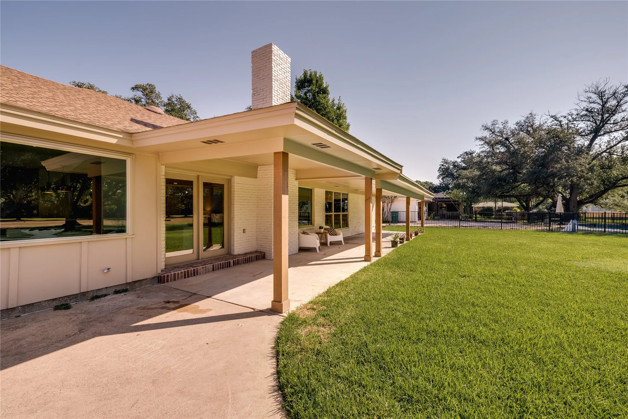 Expansive rear yard featuring a covered patio with wood columns, a large lawn area, and mature trees