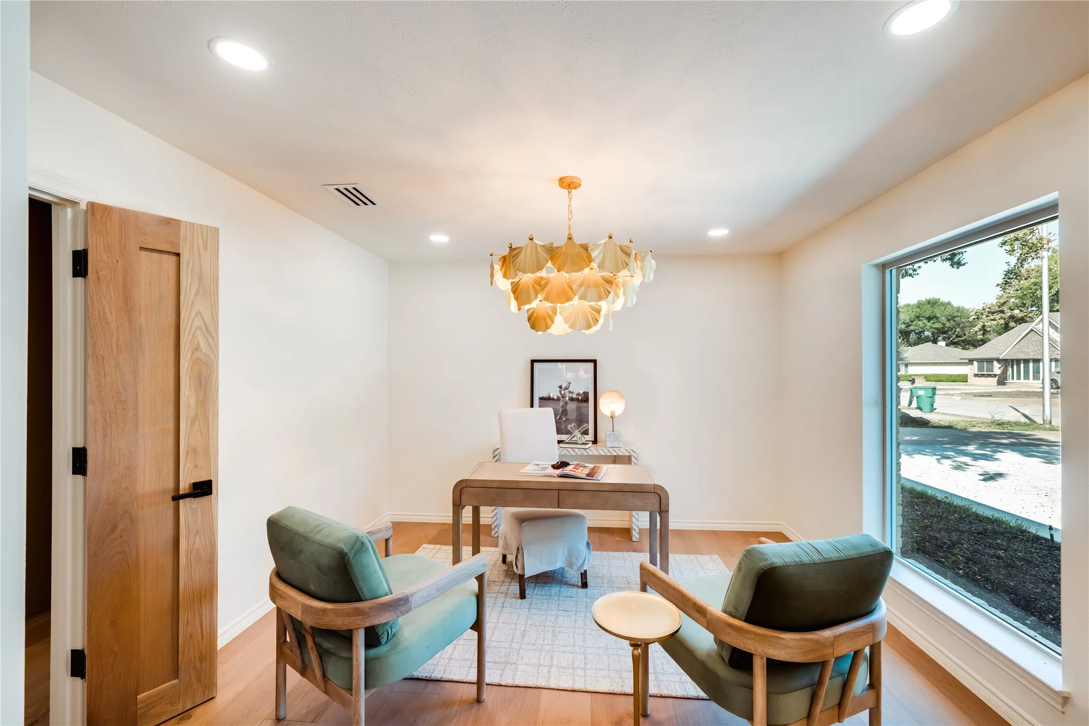 Bright interior space featuring a single-panel wood door with black hardware, recessed lighting, and wood-finish flooring