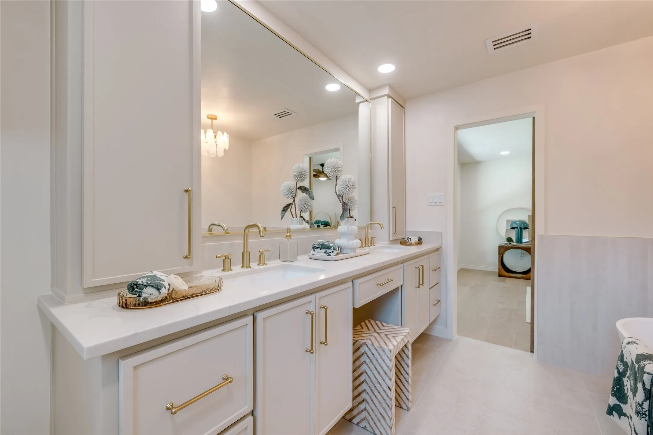 Dual vanity with integrated sinks, white cabinetry, gold-finish hardware, and a full-width mirror