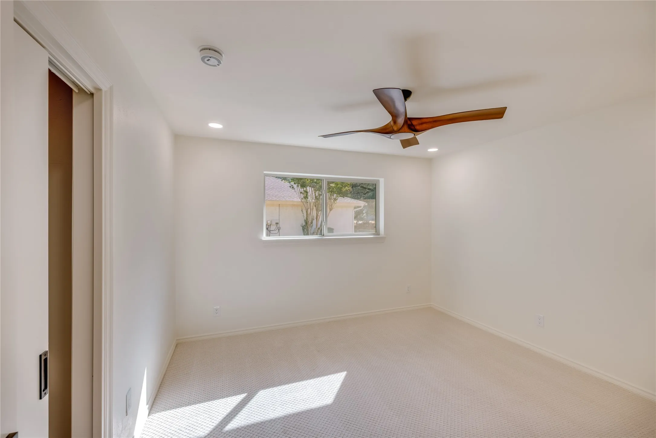 Carpeted room with a rectangular window, a ceiling fan with wood-finish blades, and recessed lighting