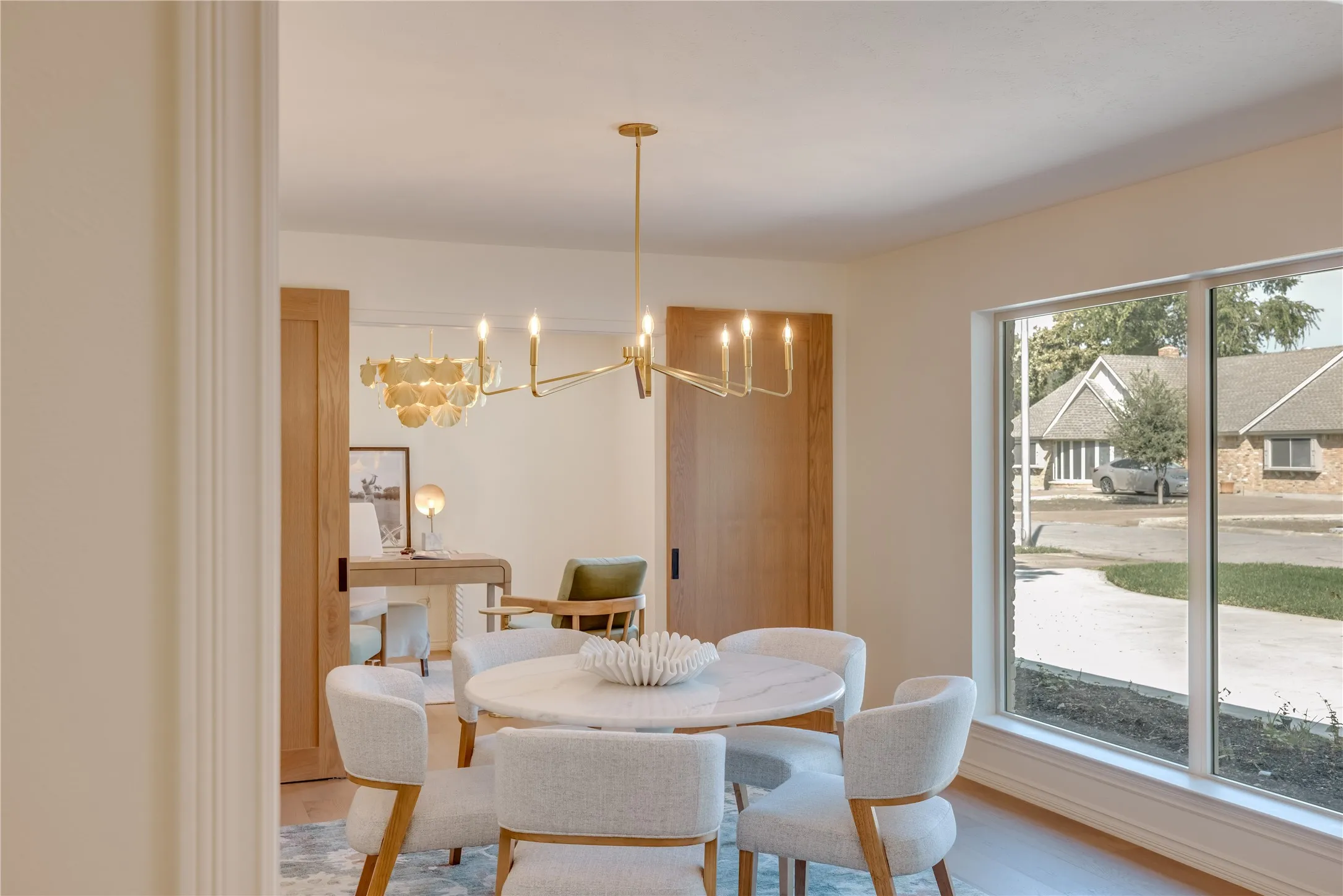 Dining area featuring a contemporary chandelier, large picture window, light wood-finish flooring, and a cased opening to an additional room